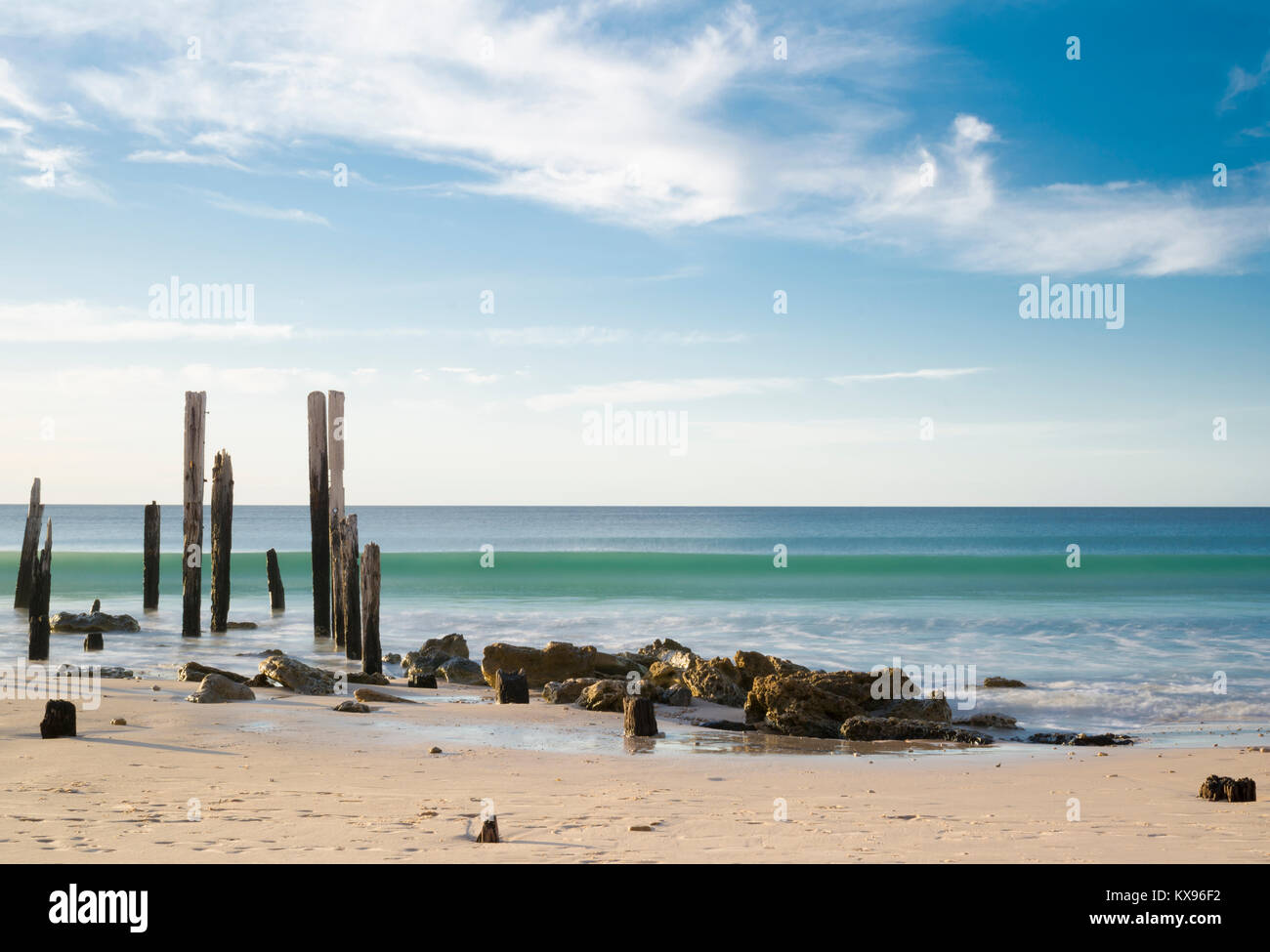 Porto Willunga Beach con il molo iconico rovine nella luce del giorno con una lenta velocità di otturatore accentuando la lunga ondata di rotolamento in arrivo. Trova i Foto Stock