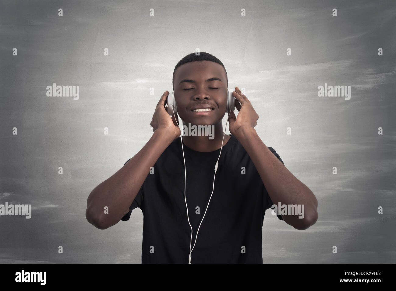 Felice l'uomo africano sorridente ascoltando la musica nelle cuffie. Sfondo grigio. Foto Stock