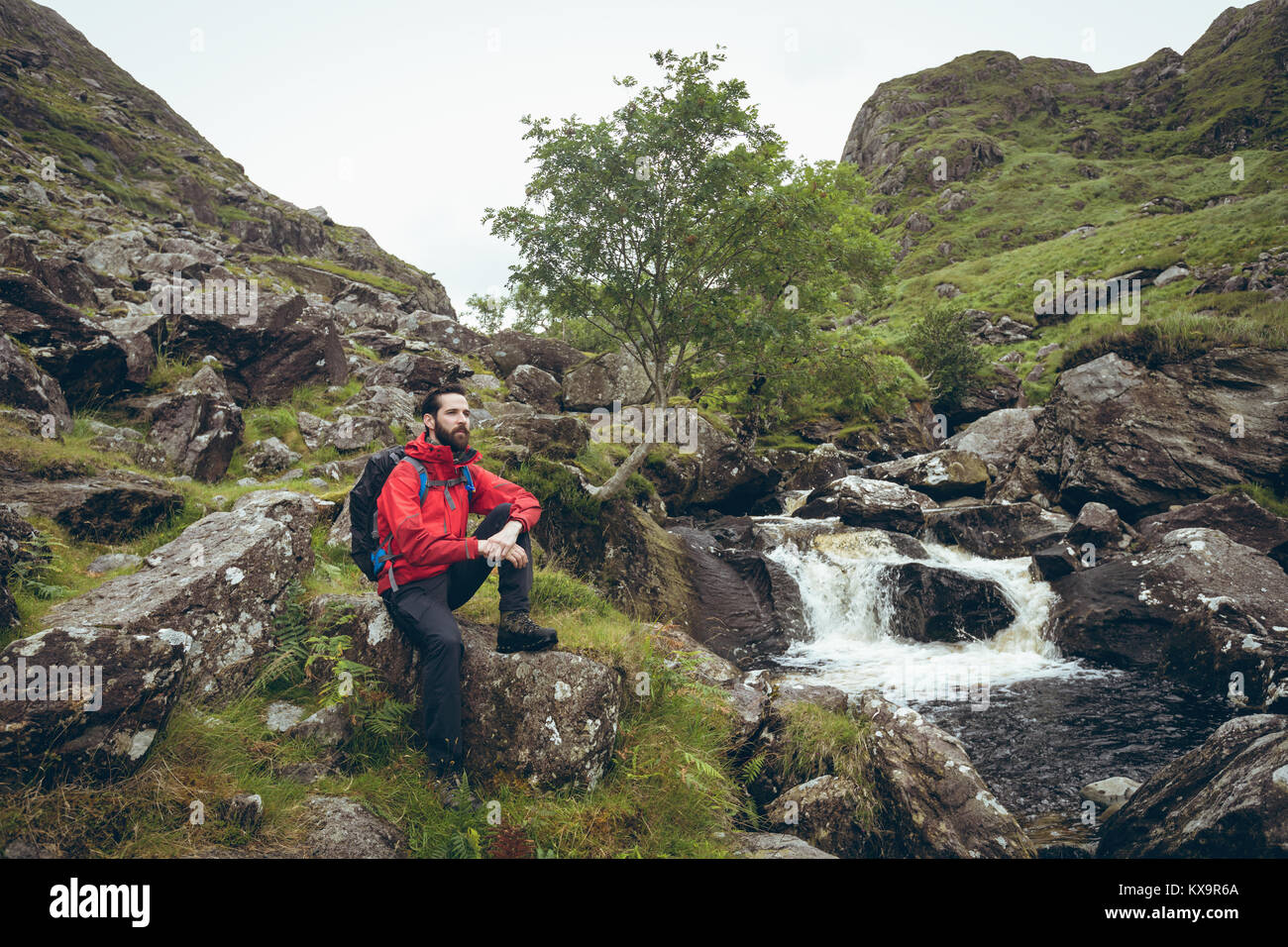 Escursionista seduto sulla roccia nei pressi di flusso Foto Stock