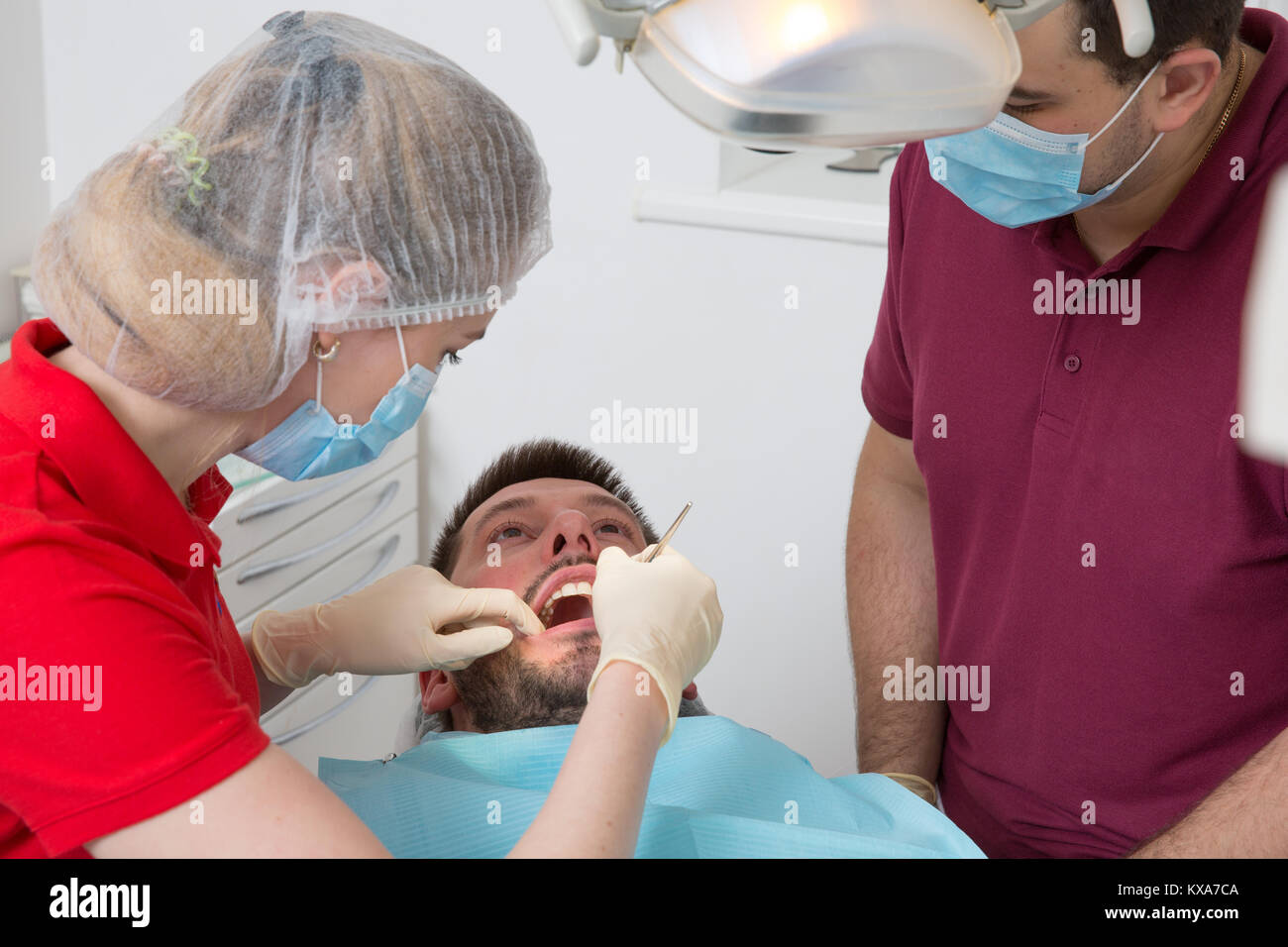 Dentista femmina con maschio assistant esaminando uomo denti del paziente presso la clinica medica o in ufficio Foto Stock