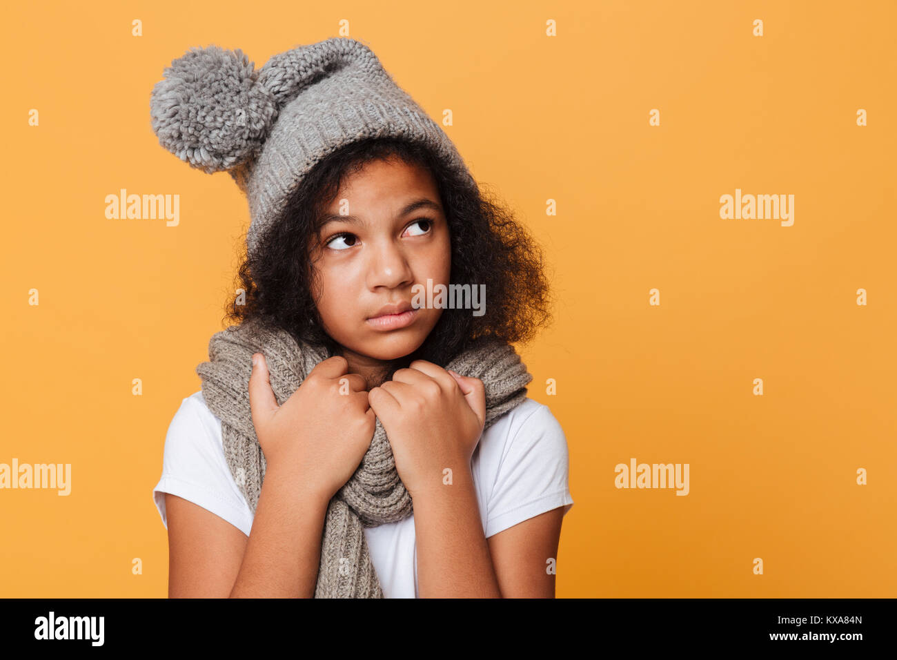 Close up ritratto di congelati afro american girl vestito con sciarpa e un cappello che guarda lontano a copiare spazio isolato su sfondo arancione Foto Stock