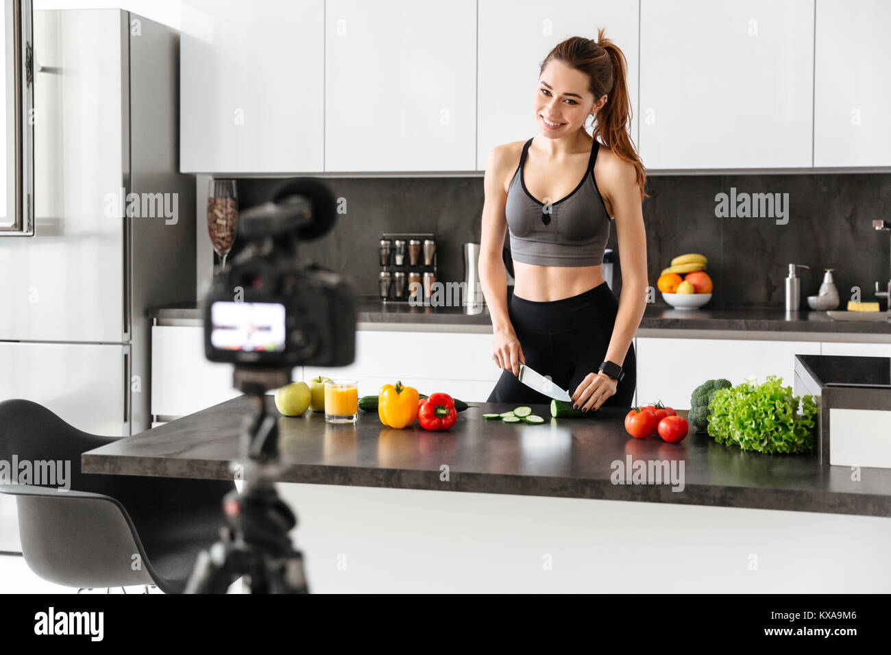 Allegro sano giovane ragazza registrazione del suo blog episodio su di una sana dieta alimentare mentre si sta in piedi in cucina a casa Foto Stock