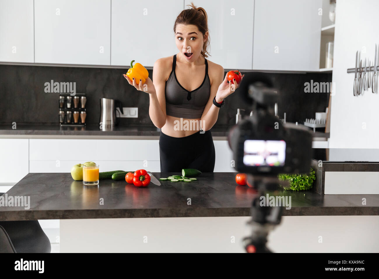 Emozionato sano giovane ragazza registrazione del suo blog episodio su di una sana dieta alimentare mentre si sta in piedi in cucina a casa Foto Stock