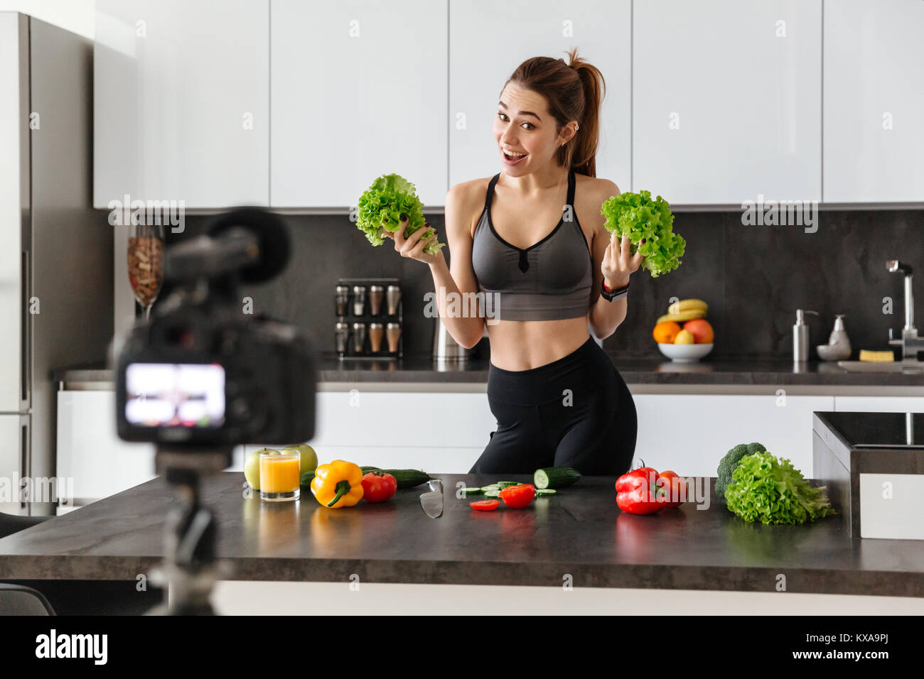 Allegro sano giovane ragazza registrazione del suo blog episodio su di una sana dieta alimentare mentre si sta in piedi in cucina a casa Foto Stock