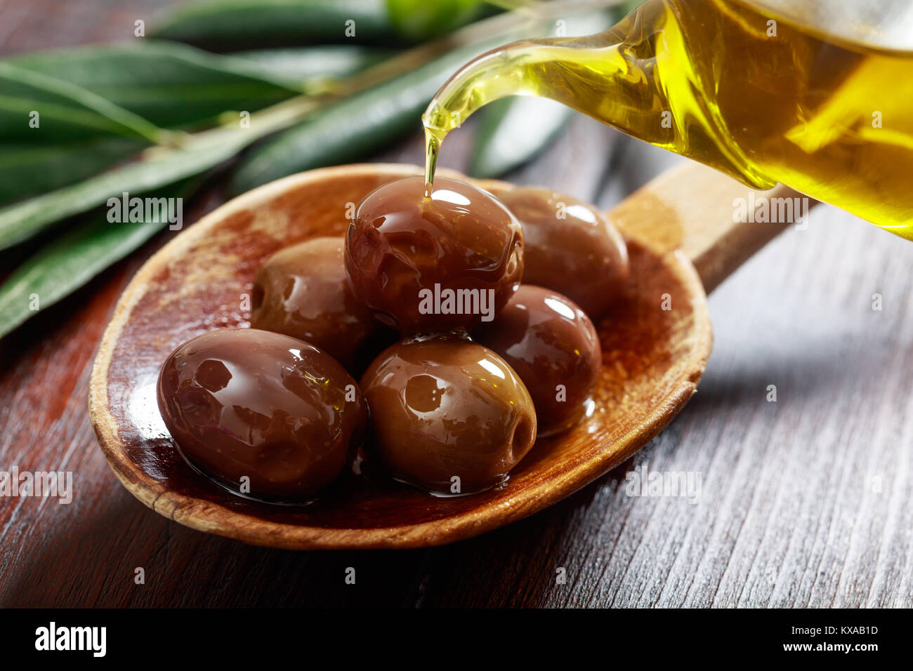 Le olive in un cucchiaio di legno e olio di oliva Foto Stock