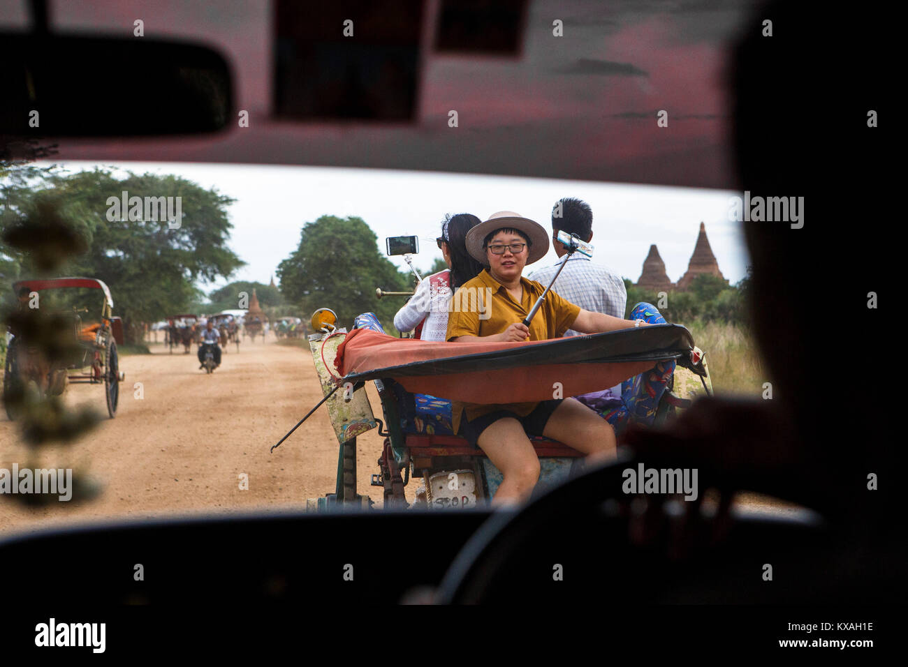 Vista dall'interno auto di turisti asiatici utilizzando bastoncini selfie a prendere le foto dello smartphone da un cavallo carrello come loro cavalcata verso un tempio buddista a Bagan, Mandalay Regione, Myanmar. Il sito è uno dei più famosi turisti destinazioni nel sud-est del paese asiatico. Foto Stock