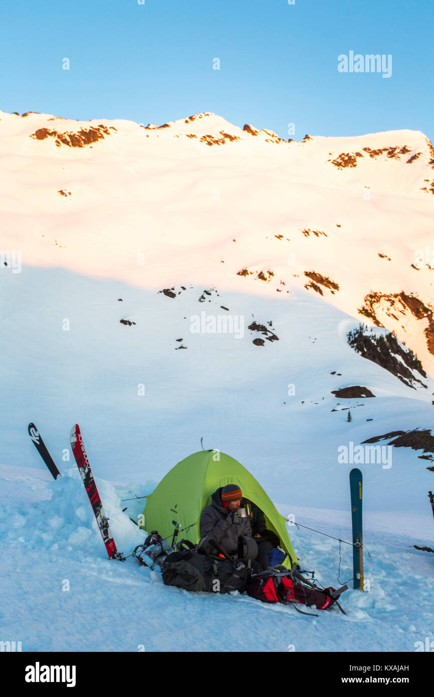 Due gli sciatori rilassante in tenda si accamparono sulla collina innevate all'alba, Leavenworth, Washington, Stati Uniti d'America Foto Stock