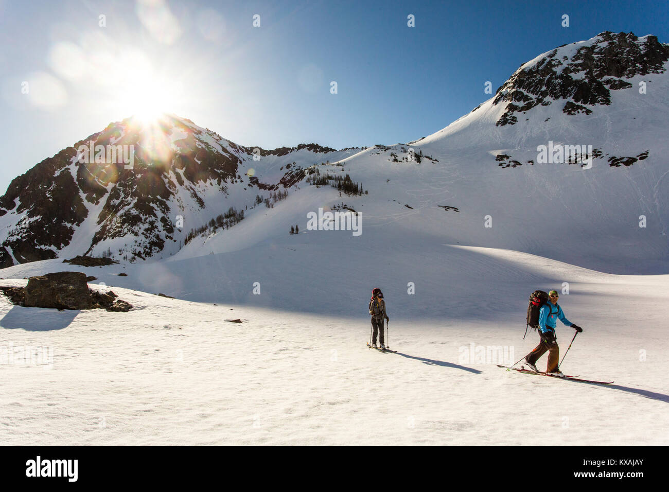 Due sciatori in attraversamento backcountry aprire pendio soleggiato sotto il cielo blu, Leavenworth, Washington, Stati Uniti d'America Foto Stock