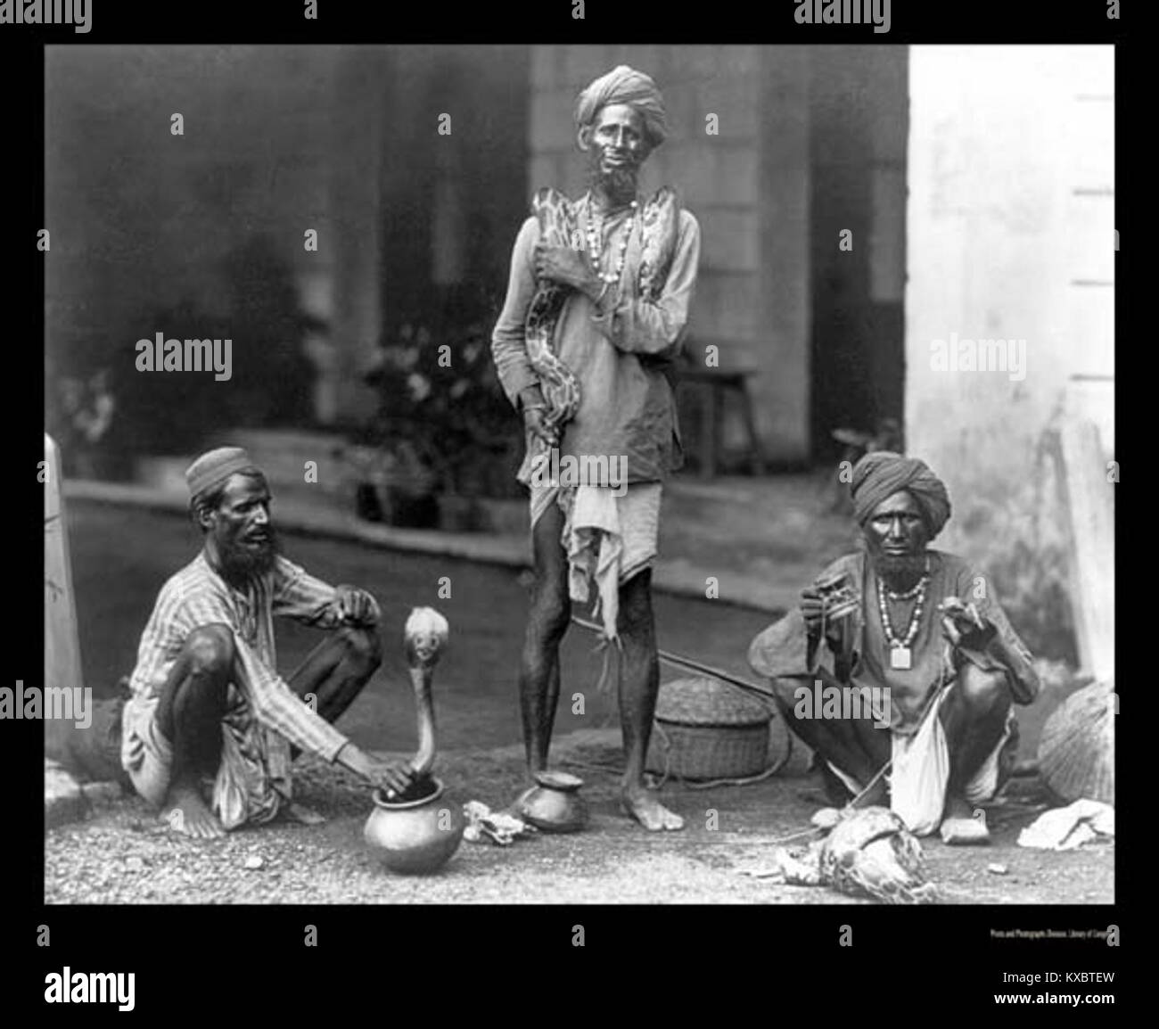 Questa fotografia del 1898 cattura gli incantatori di serpenti in azione, mostrando la pratica tradizionale di utilizzare la musica per attirare e controllare i serpenti. L'immagine fornisce uno sguardo sulle pratiche culturali e l'intrattenimento nel tardo XIX secolo, evidenziando in particolare la relazione tra esseri umani e rettili. Foto Stock