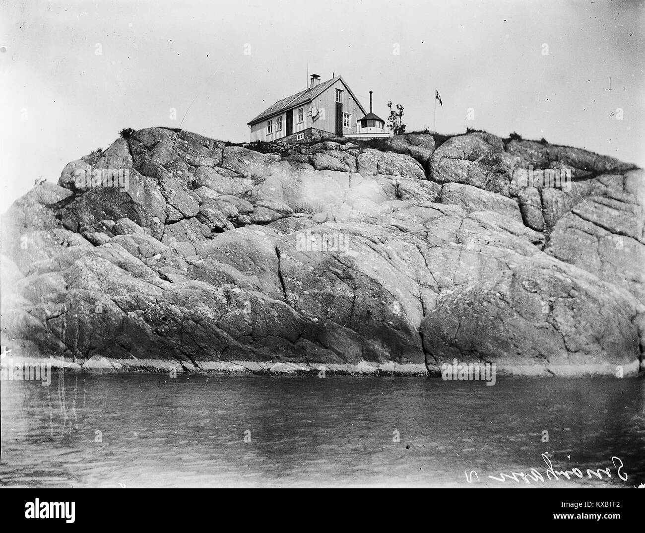 La fotografia “Smørhavn, Bremanger – S-1602U2 038” raffigura l’insediamento costiero di Smørhavn nel comune di Bremanger, Norvegia, che mostra capanne per la pesca, case sul lungomare e litorale dei fiordi in un contesto norvegese occidentale. Foto Stock
