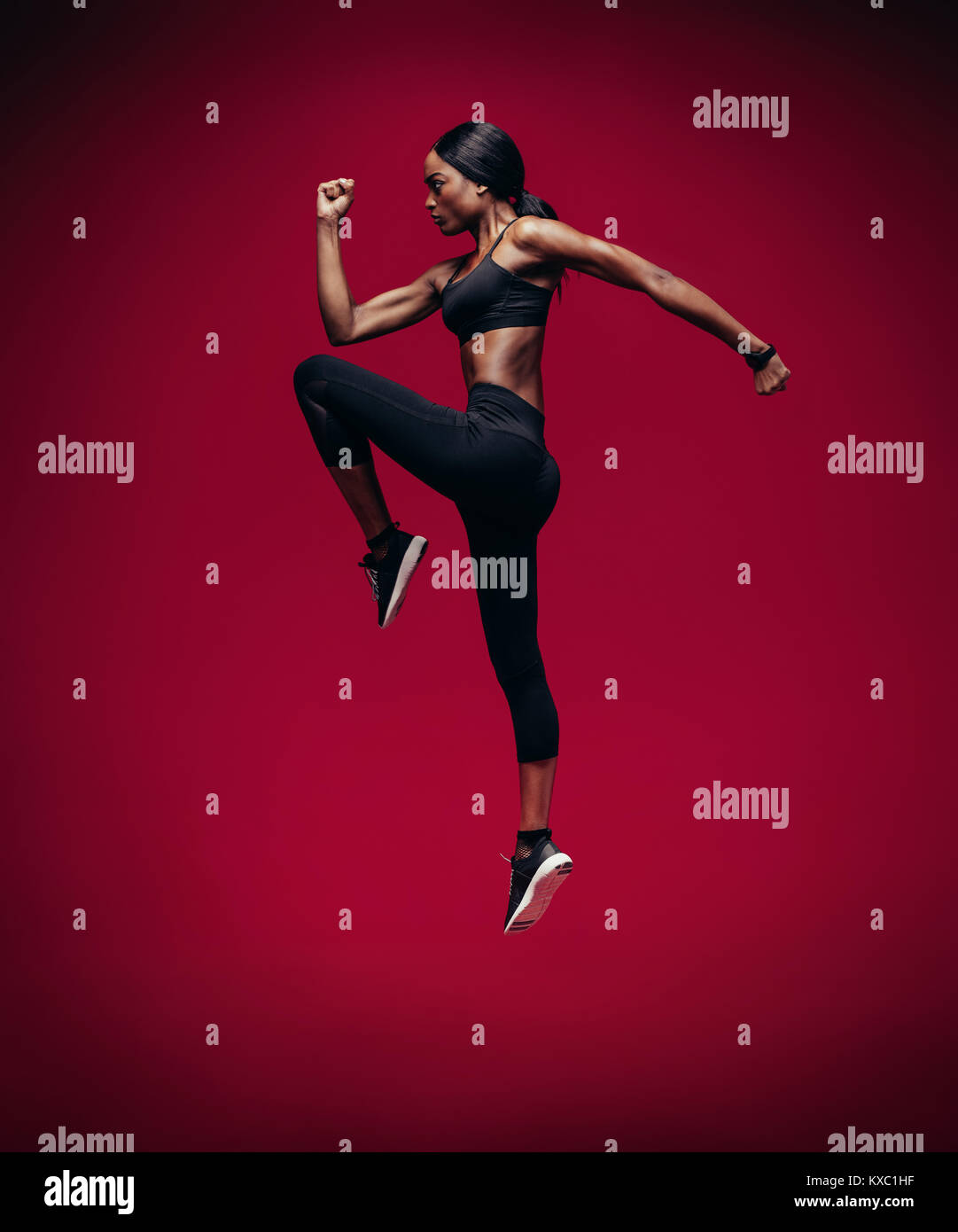 African atleta femminile di salto e allungando su sfondo rosso. Una sana e robusta donna di esercizio. Foto Stock