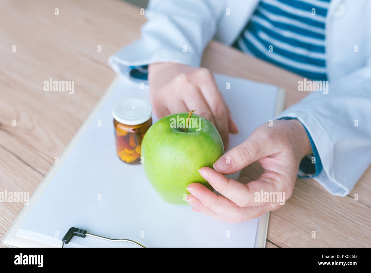 Consulenza medico Apple invece di pillole e antibiotici, mani femminili in camice bianco con frutta verde in modo favorevole per raggiungere e mantenere sana l Foto Stock