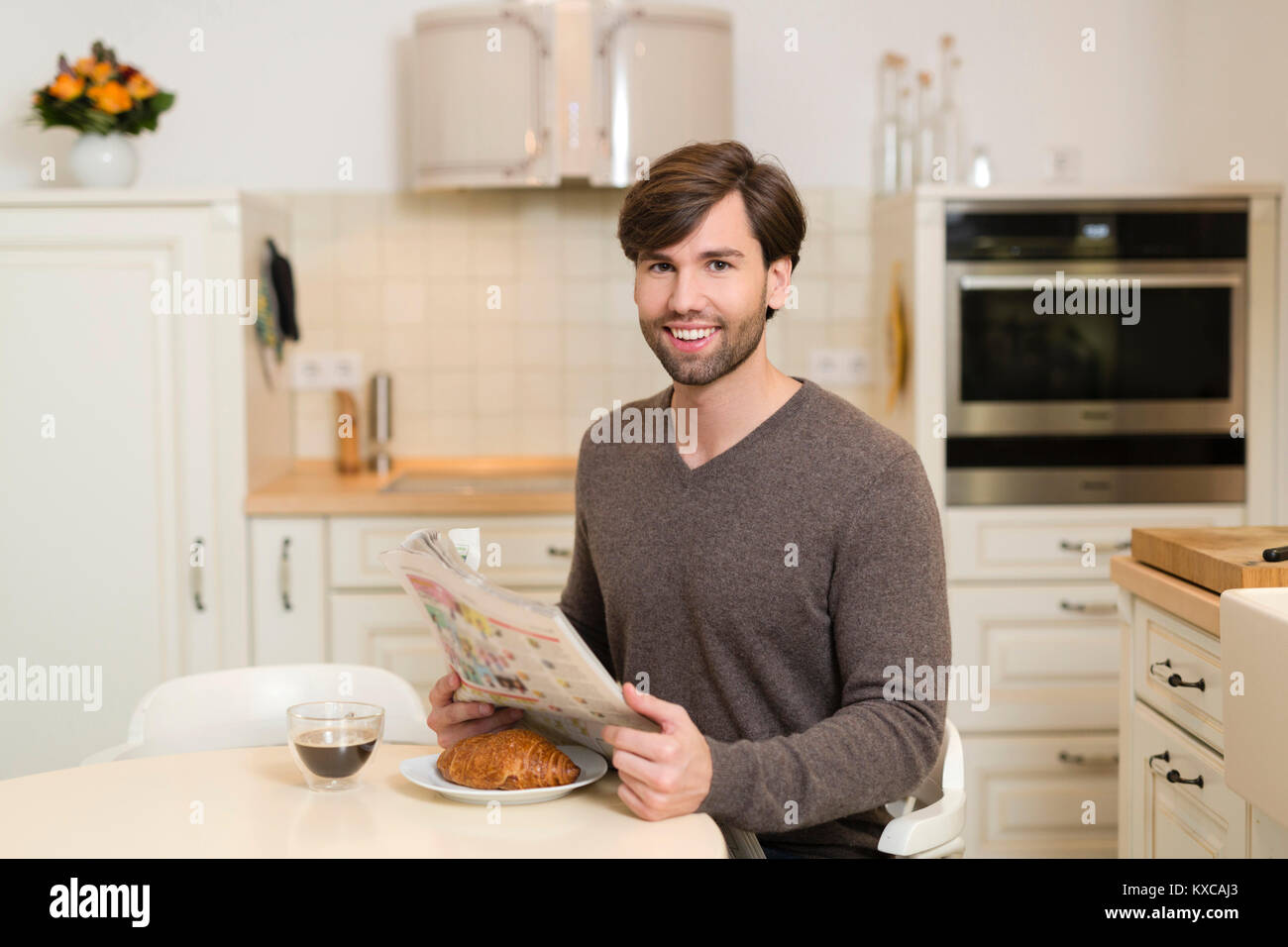 Ritratto di uomo sorridente seduti al tavolo per la colazione con quotidiano Foto Stock