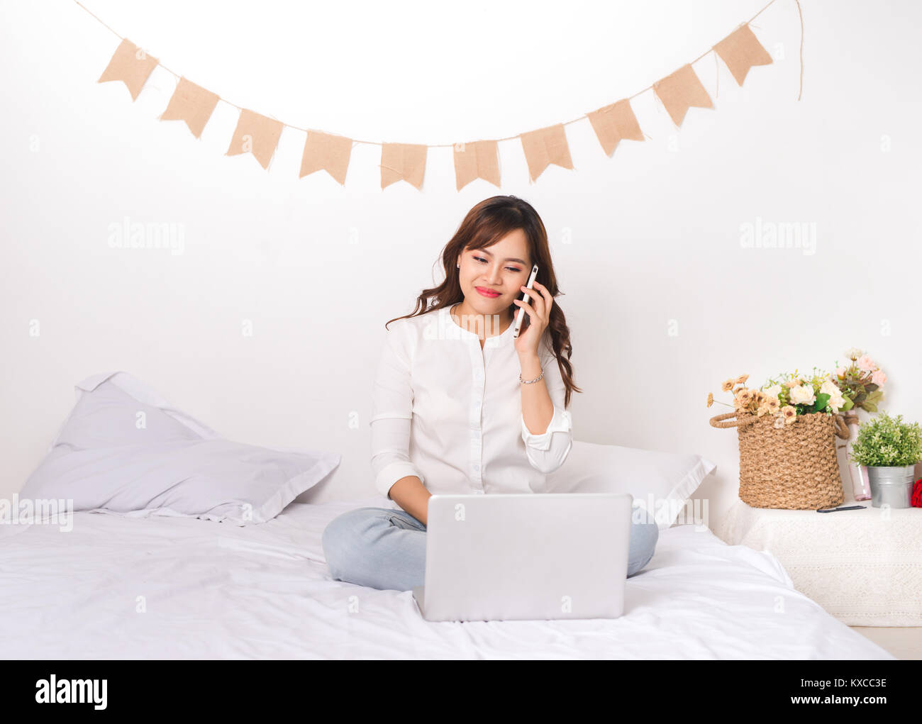 Asian lady in abito classico sta parlando al telefono cellulare e di lavoro sul portatile a casa Foto Stock