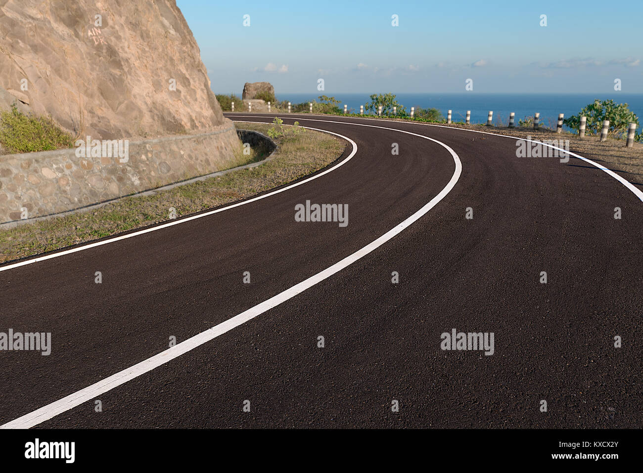 Asfalto strada costiera intorno a bordo scogliera curva, con il mare blu back drop. Foto Stock
