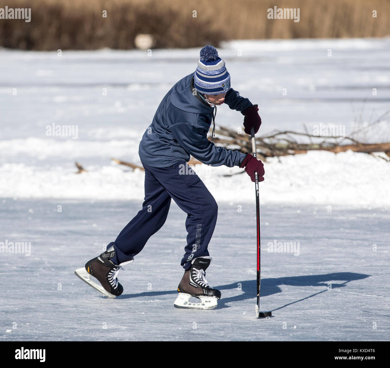 Ragazzo adolescente che gioca a hockey su ghiaccio in un laghetto in una fredda giornata invernale Foto Stock