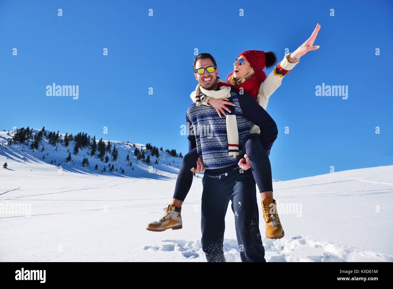 Coppia giovane divertirsi sulla neve. Felice l'uomo alla montagna dando piggyback ride per la sua ragazza sorridente. Foto Stock