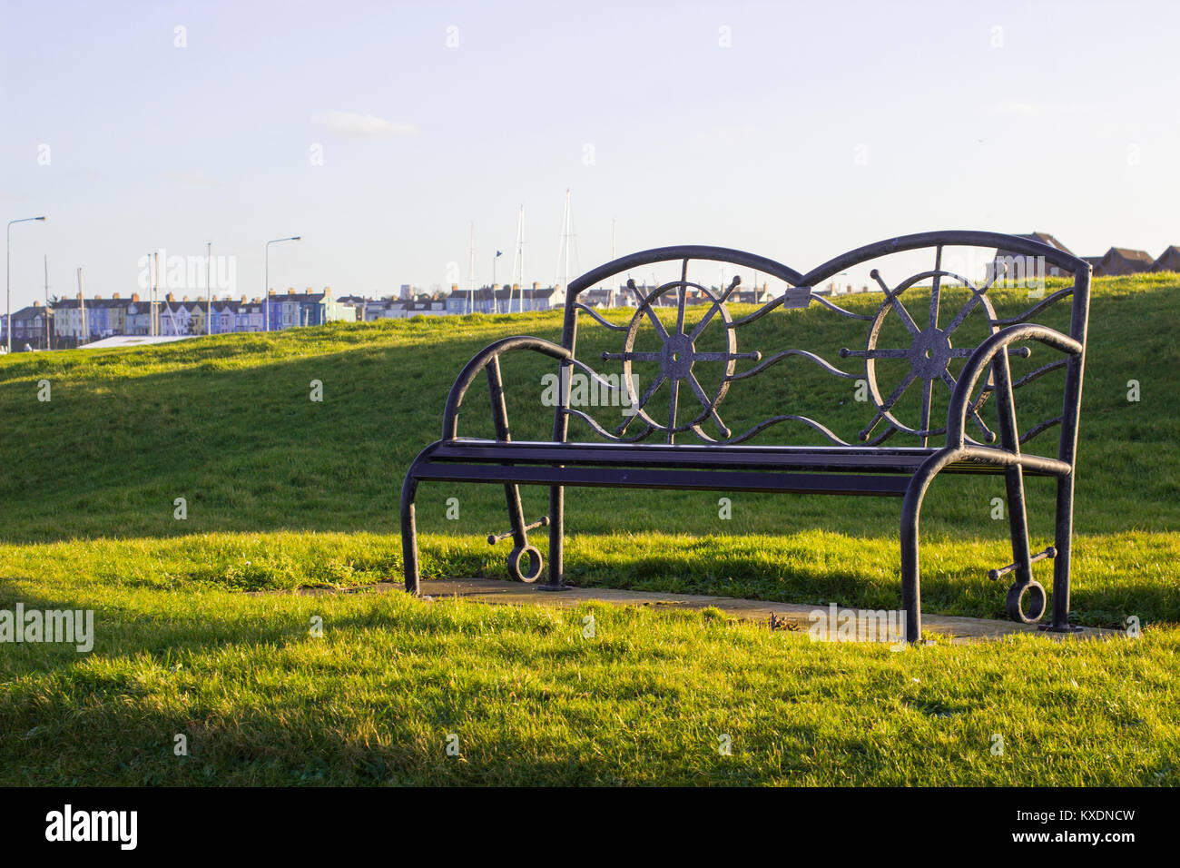 Una polvere di metallo rivestito di una panchina nel parco in un design contemporaneo retroilluminata con la luce soffusa del sole invernale Foto Stock