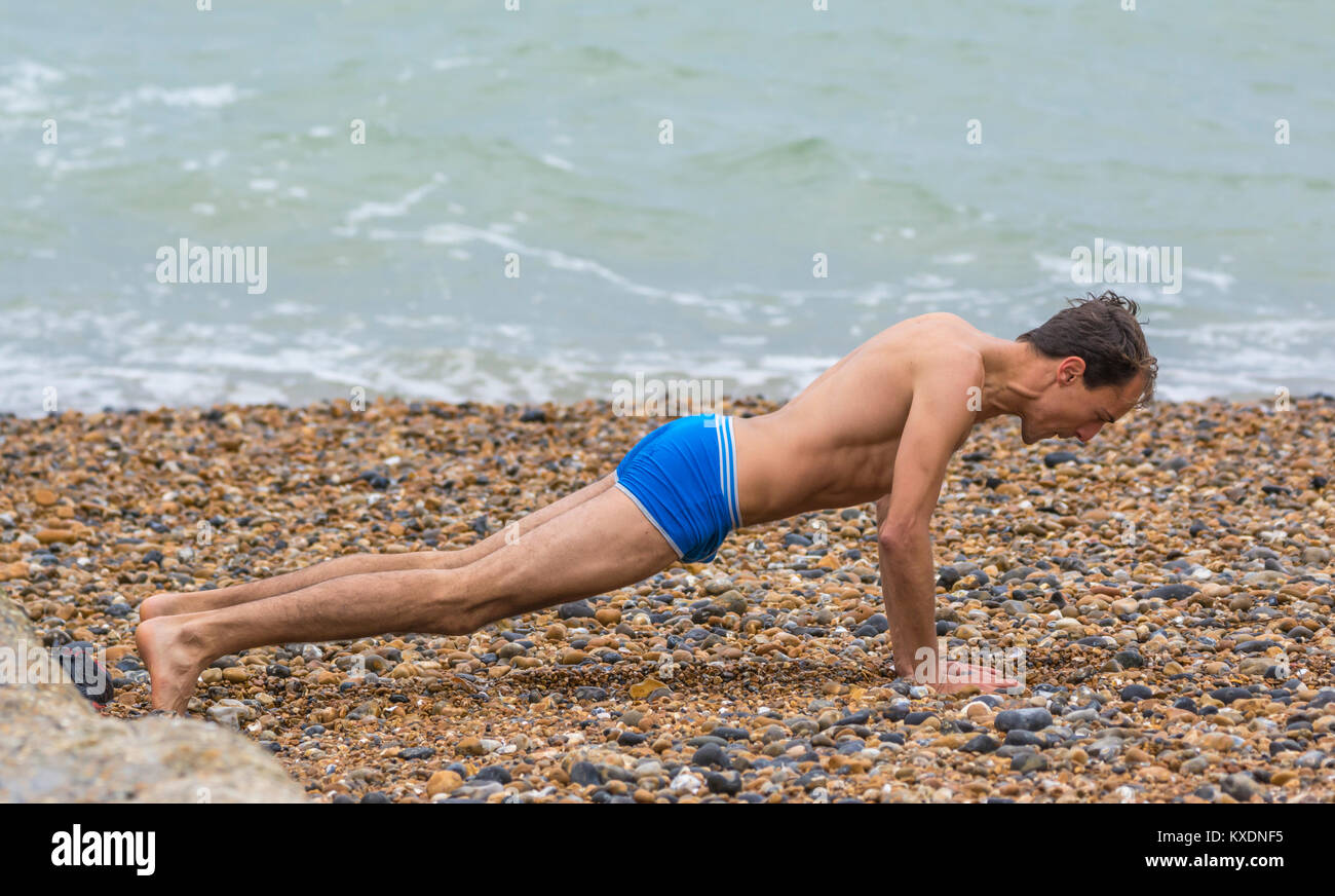 Uomo che indossa solo shorts facendo esercizi del mattino (pushups, push ups, pressups, premere ups) su una spiaggia in un freddo giorno nel Regno Unito. Foto Stock