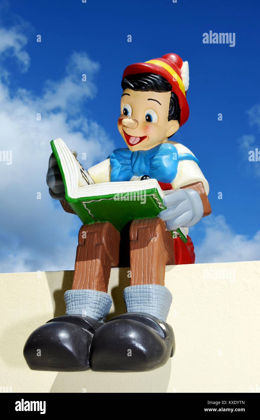 Pinocchio figura seduta su un plympth tenendo un libro. Questa figura è parte di una grande collezione privata della vita dimensioni display Disney figure. Foto Stock