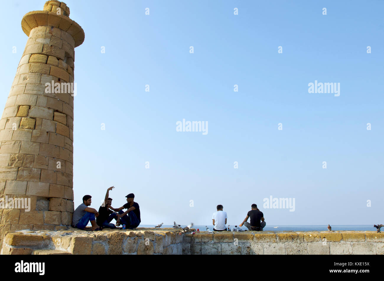 La gente del posto reaxing insieme su una parete accanto a un faro nella zona del porto di Kyrenia, Cipro Foto Stock