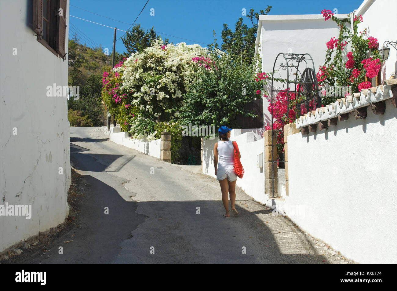 Donna che cammina giù per una strada in Karmi e godendo di fiori colorati, Cipro Foto Stock