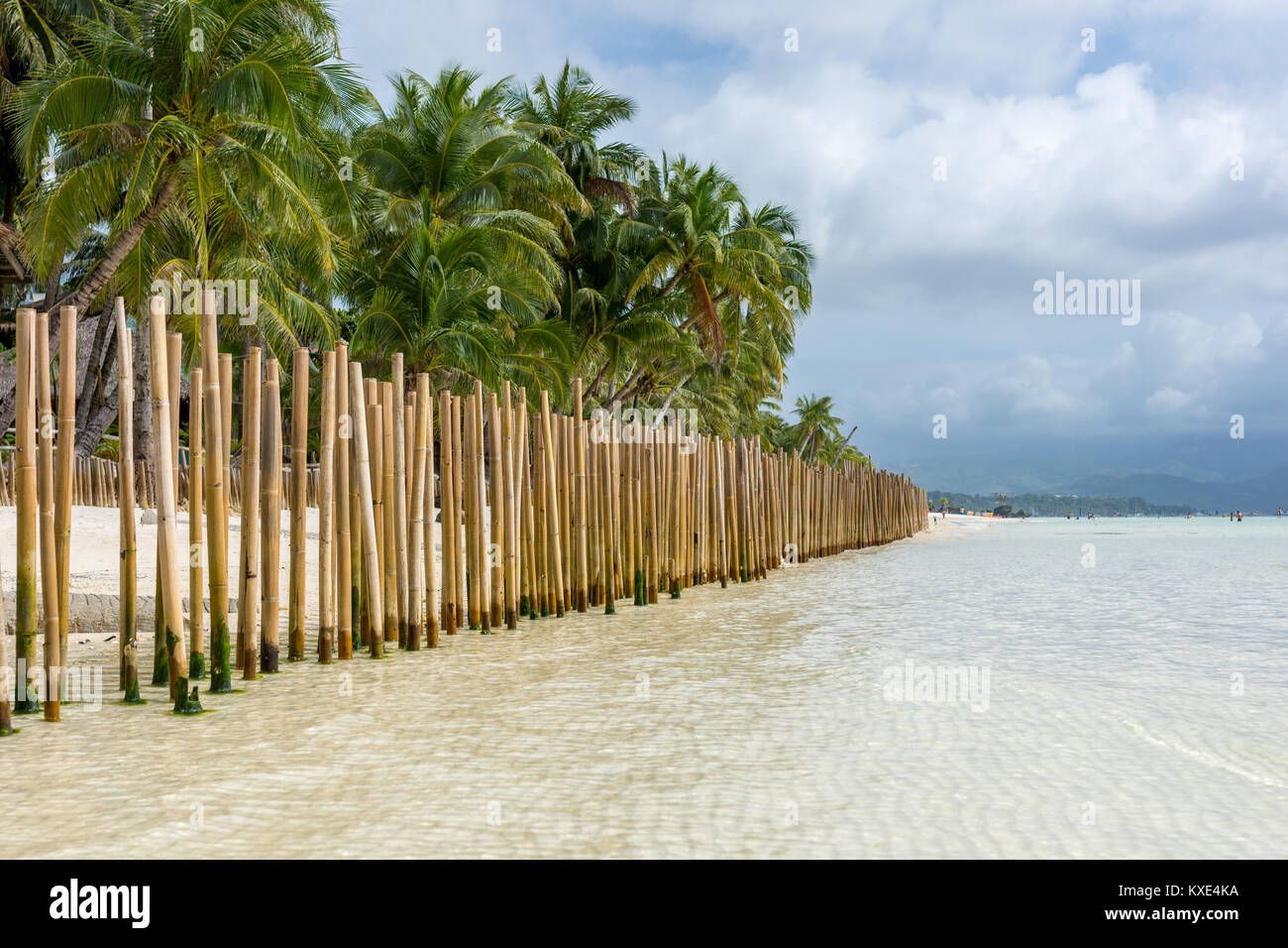 Guardando verso il basso una barriera di recinzione fatta di poli di bambù in un'isola tropicale di spiaggia di sabbia bianca con un palm alberata a riva e il promontorio collinare in distanc Foto Stock