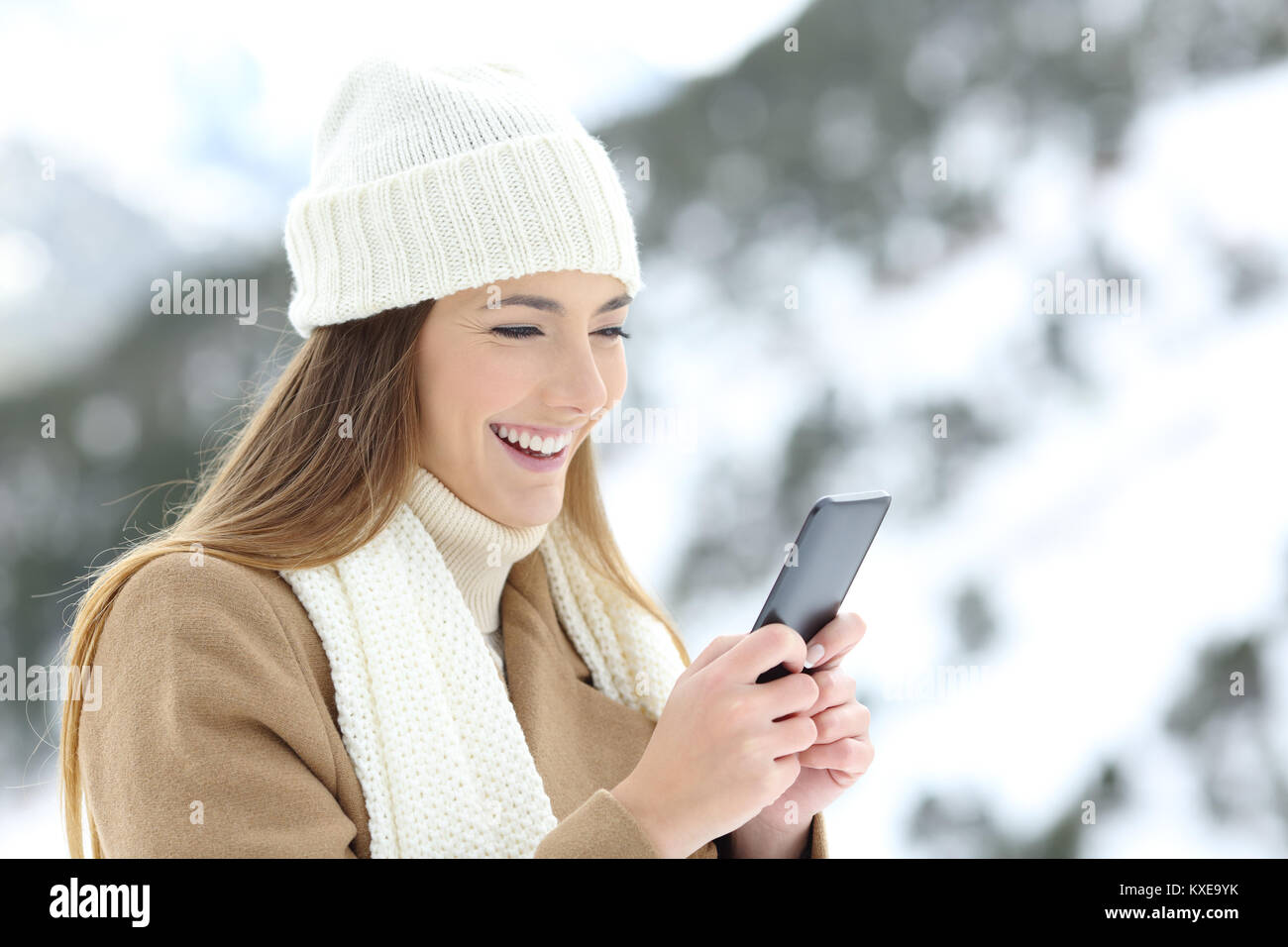Felice lady utilizzando uno smart phone in vacanze invernali in una montagna innevata Foto Stock