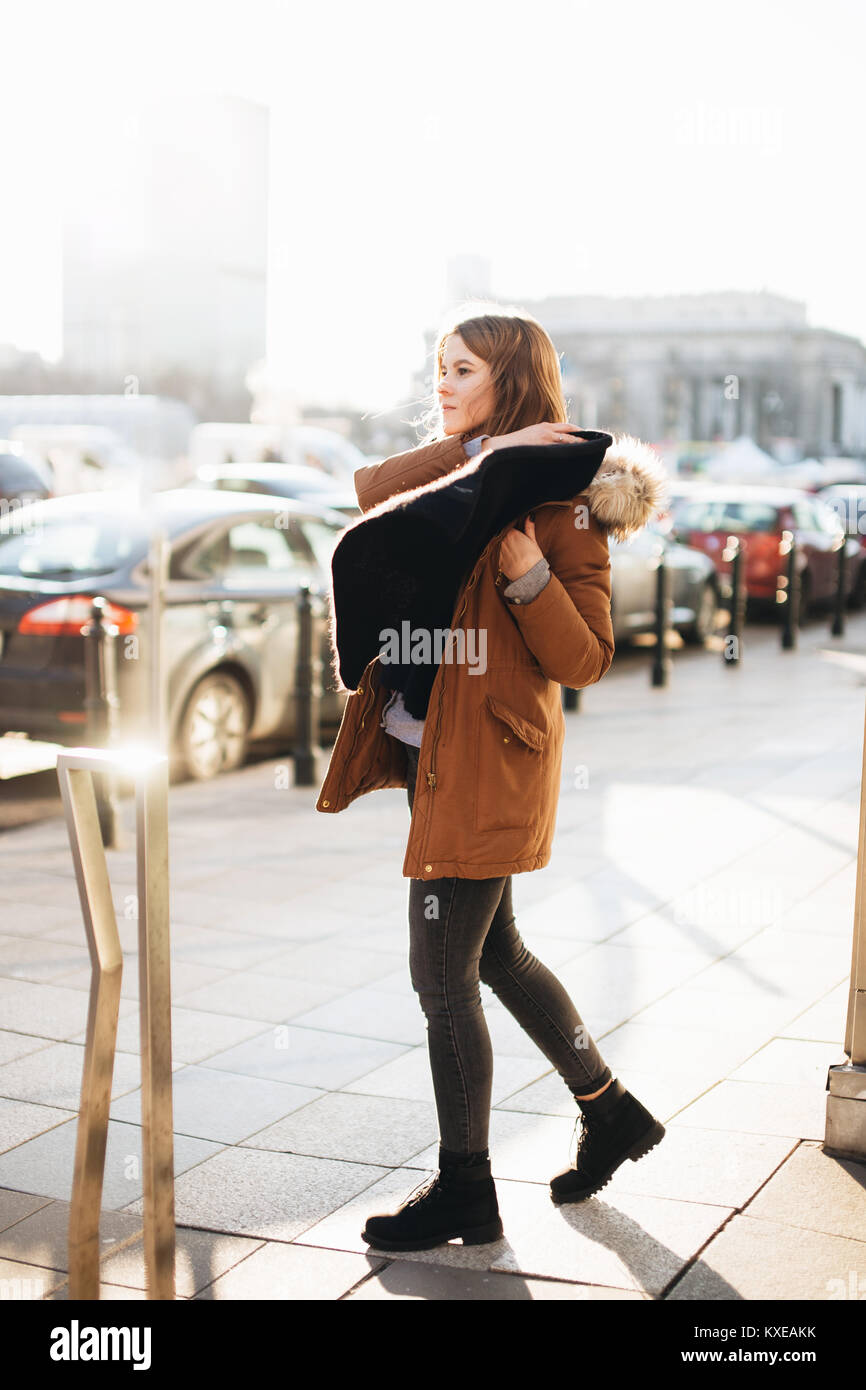 Giovane ragazza carina a piedi sulla strada. Appendere la sua sciarpa in una mano e guardarsi intorno. Abbigliamento invernale con clima caldo Foto Stock