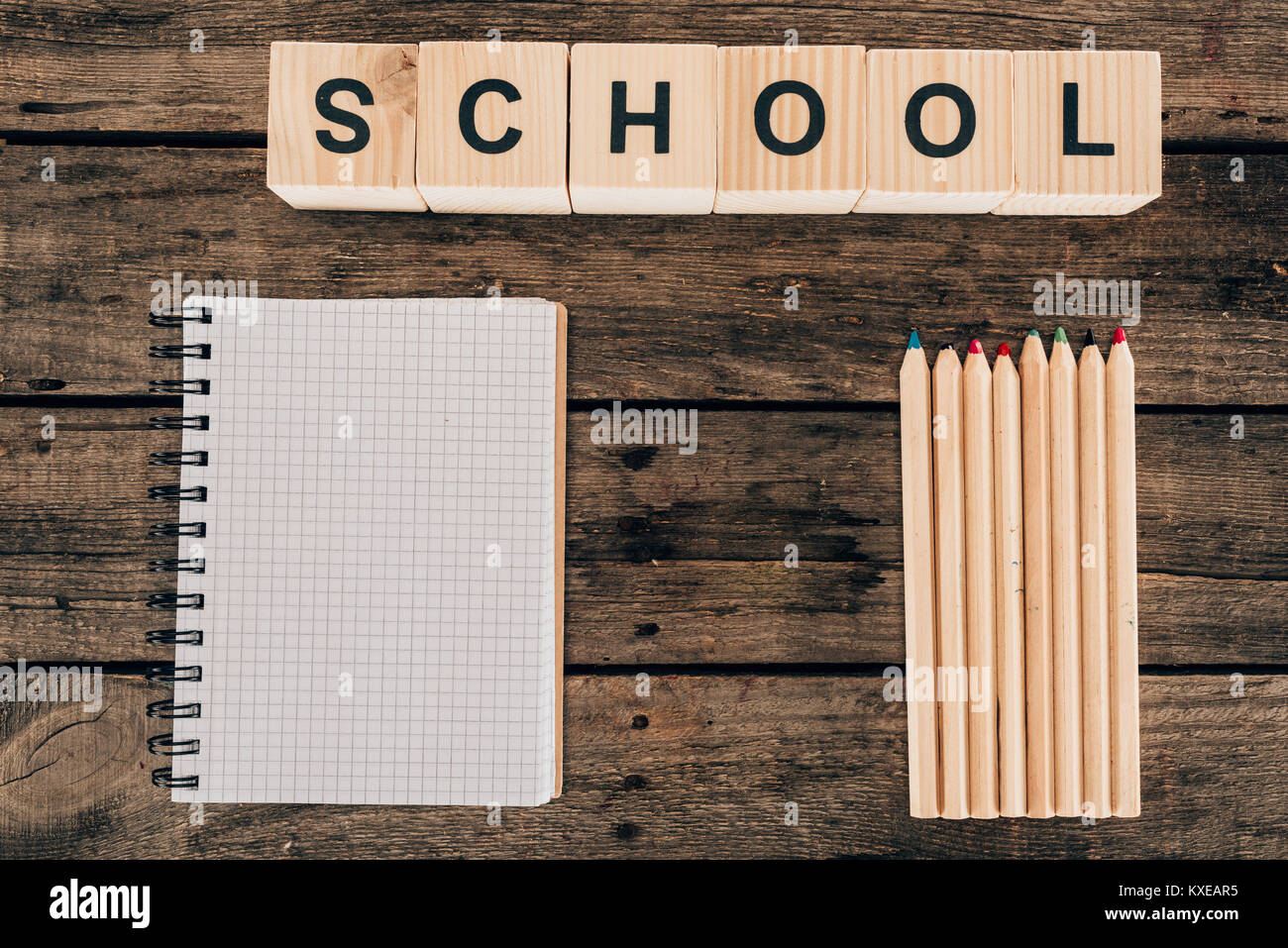 Vista superiore della composizione di matite colorate con notebook vuoto e scuola di parola su sfondo di legno Foto Stock