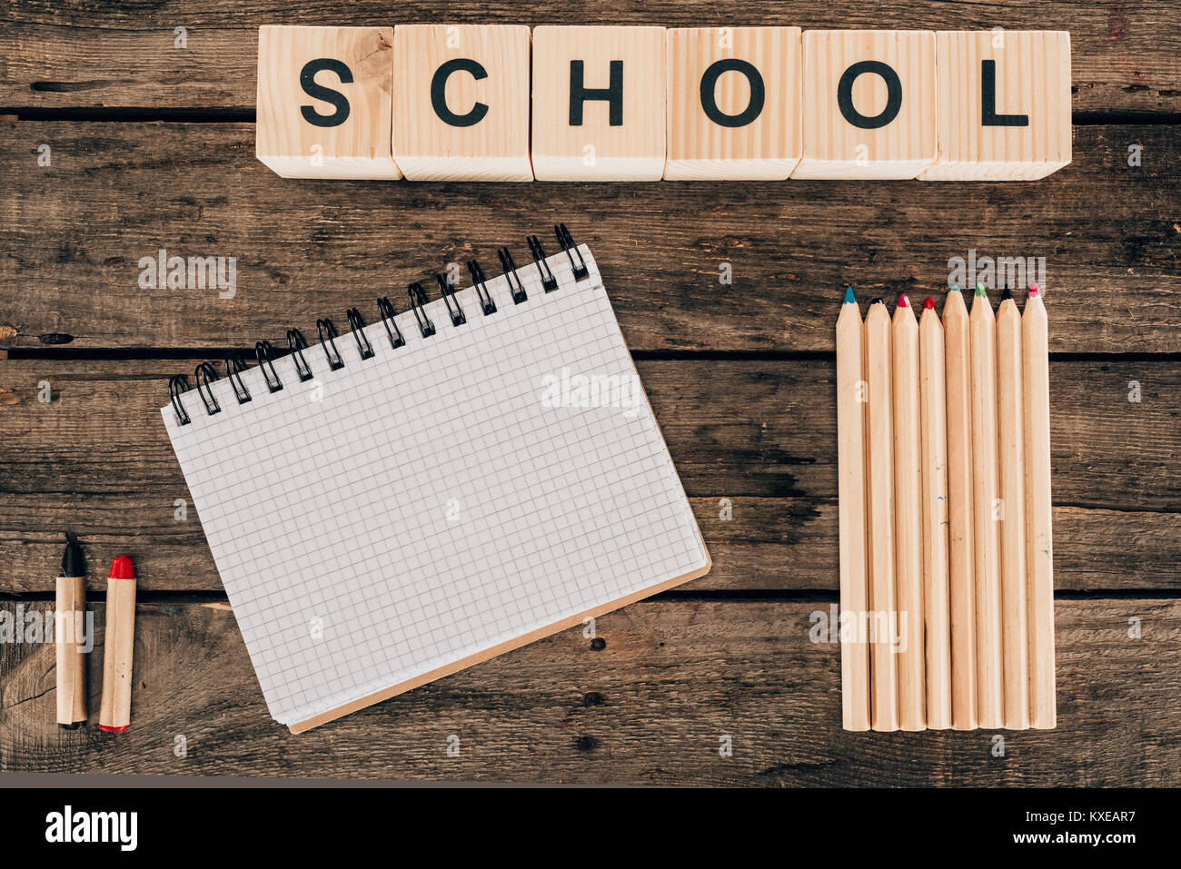 Vista superiore della composizione di matite colorate con notebook vuoto e scuola di parola su sfondo di legno Foto Stock