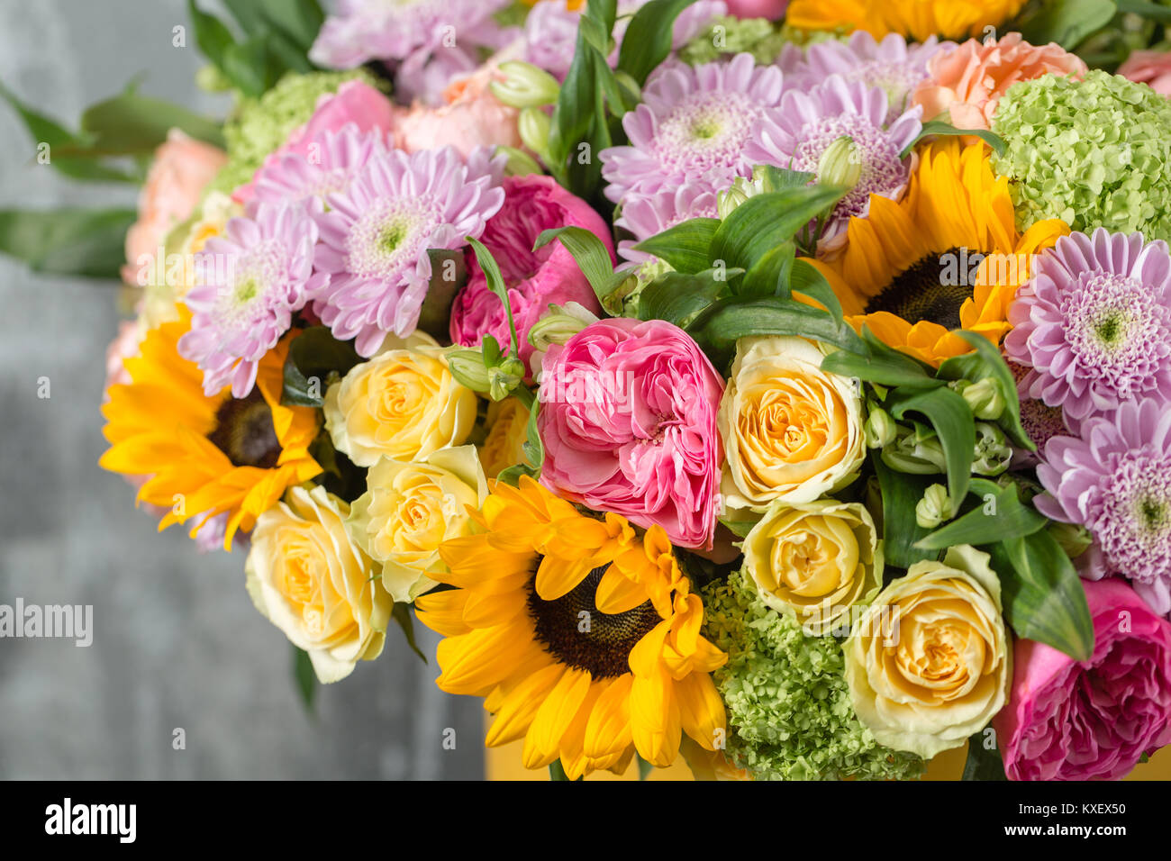 Bouquet di fiori misti in un vaso sul tavolo in legno. Il lavoro del fioraio presso un negozio di fiori. un brillante mix di girasoli, crisantemi e rose Foto Stock