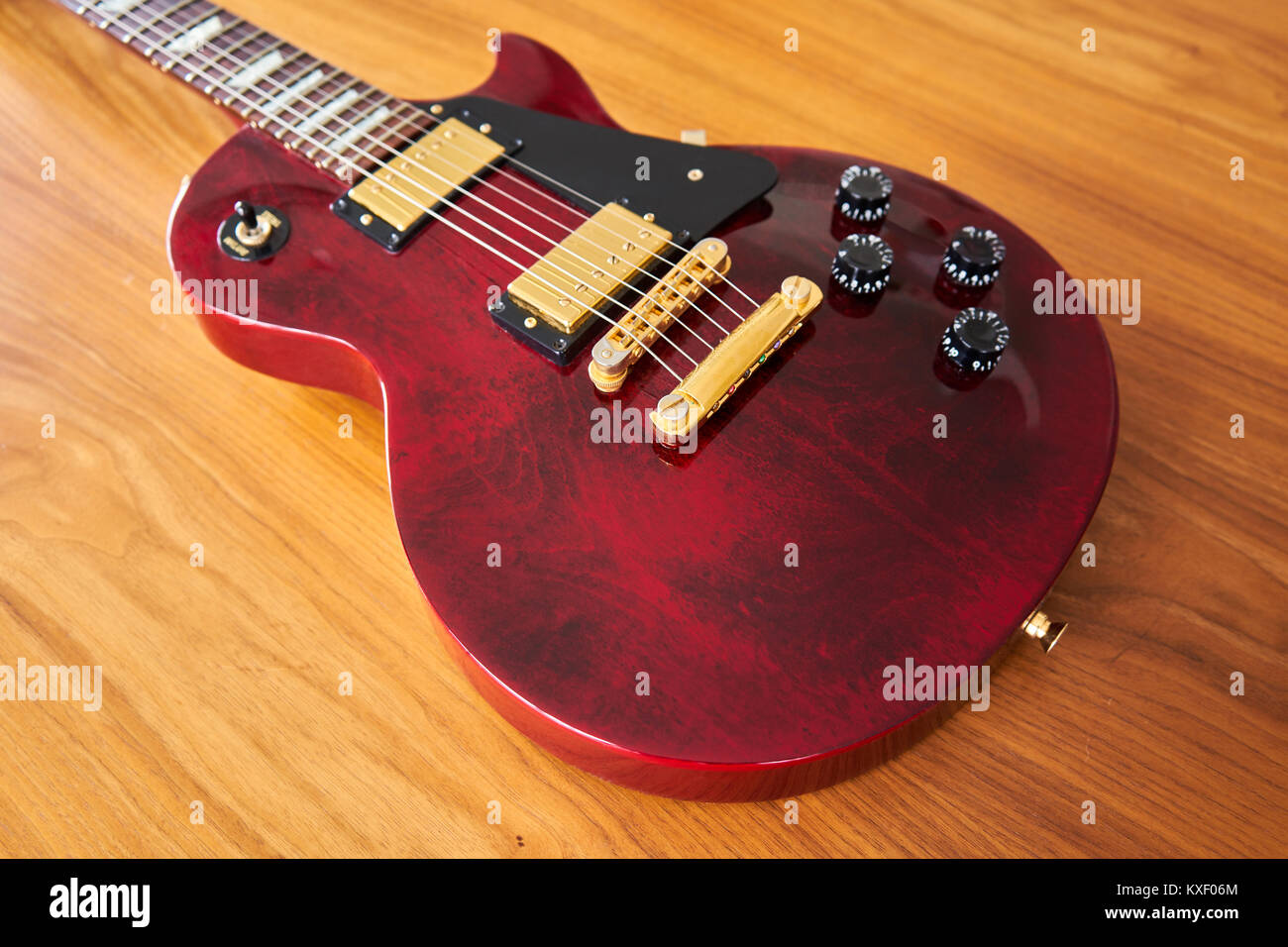 Shiny rosso vino Chitarra con Golden hardware su un tavolo di legno Vista laterale Foto Stock