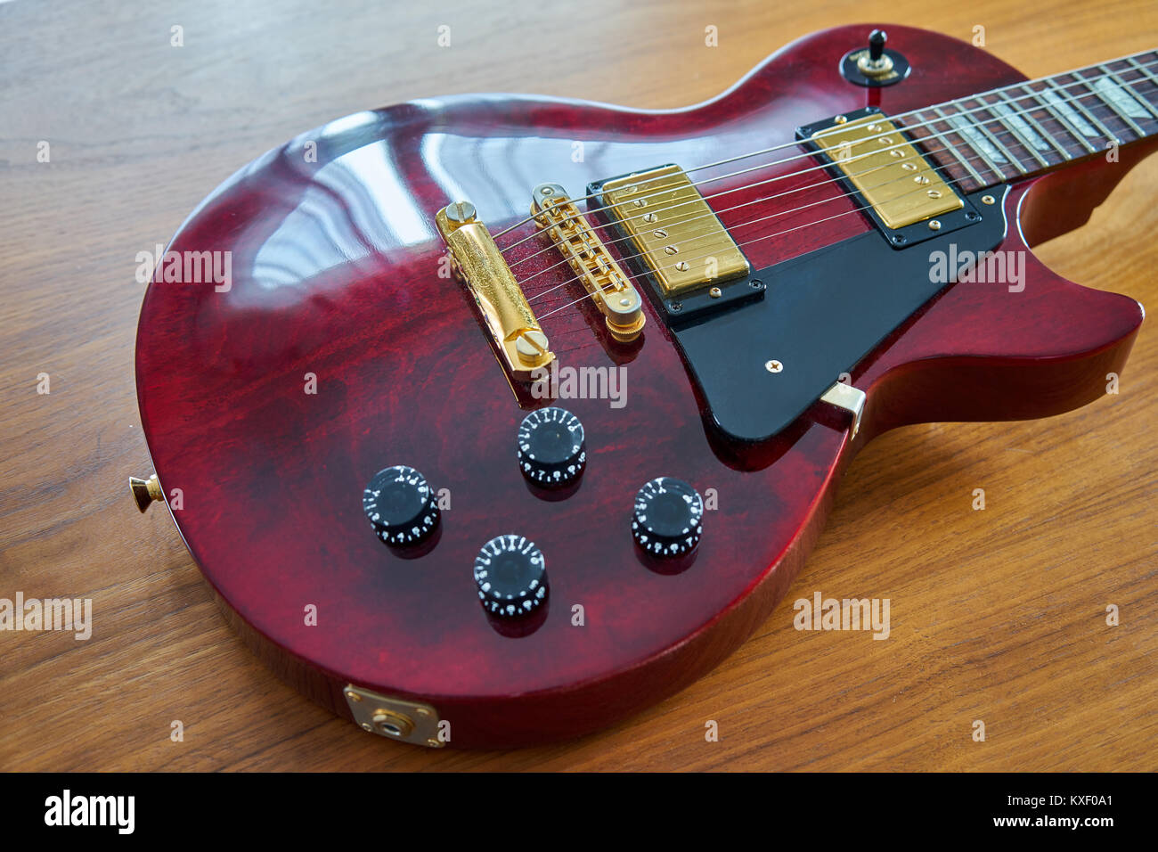 Shiny rosso vino Chitarra con Hardware dorato collocato su un tavolo in legno ad angolo vista laterale Focus sulla barra di arresto e pickup Foto Stock