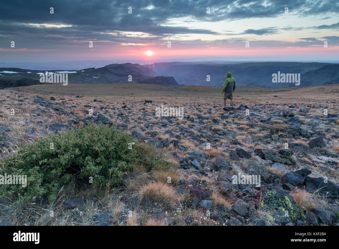 Un uomo guarda il sole che tramonta dietro le nuvole dalla cima del monte Steens, Oregon. Foto Stock