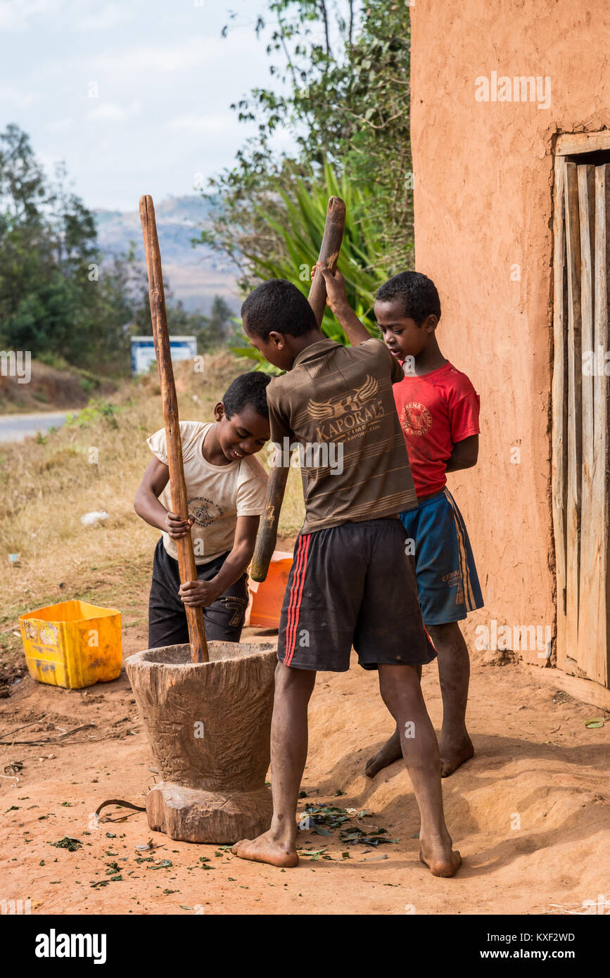 I ragazzi pounding foglie di manioca in un pestello di legno di malte, per rendere ravitoto, un tradizionale piatto malgascio. Madagascar, Africa. Foto Stock