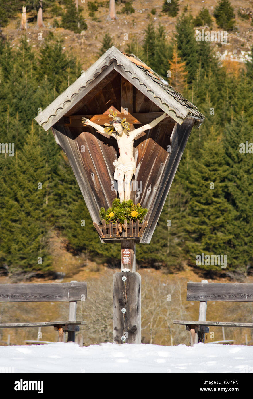 Piccolo Santuario con l'immagine di Cristo scolpito in legno con panche tipico dei sentieri di montagna con la foresta in background Foto Stock