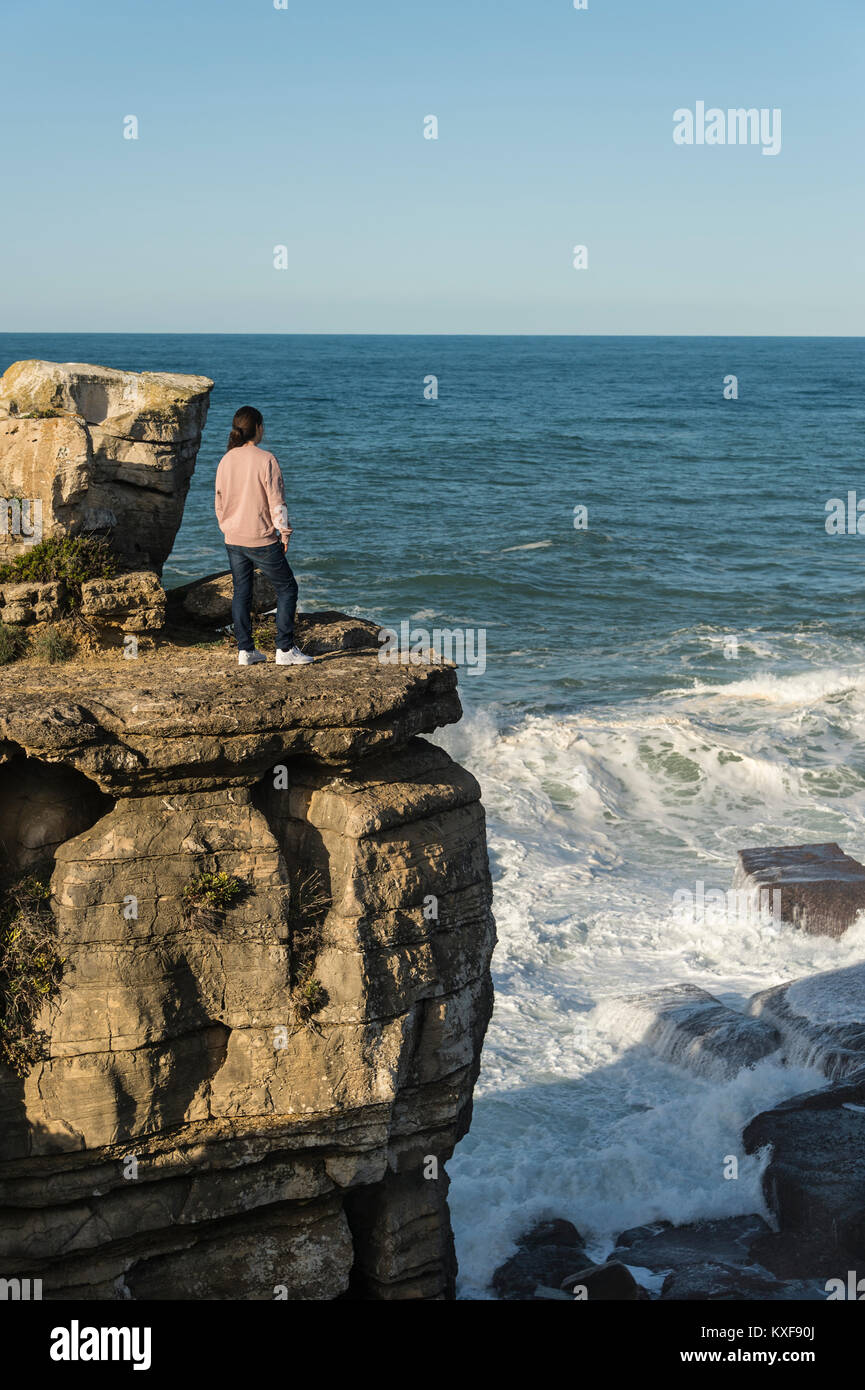 Donna in piedi sul bordo di un promontorio roccioso guardando le onde. Foto Stock