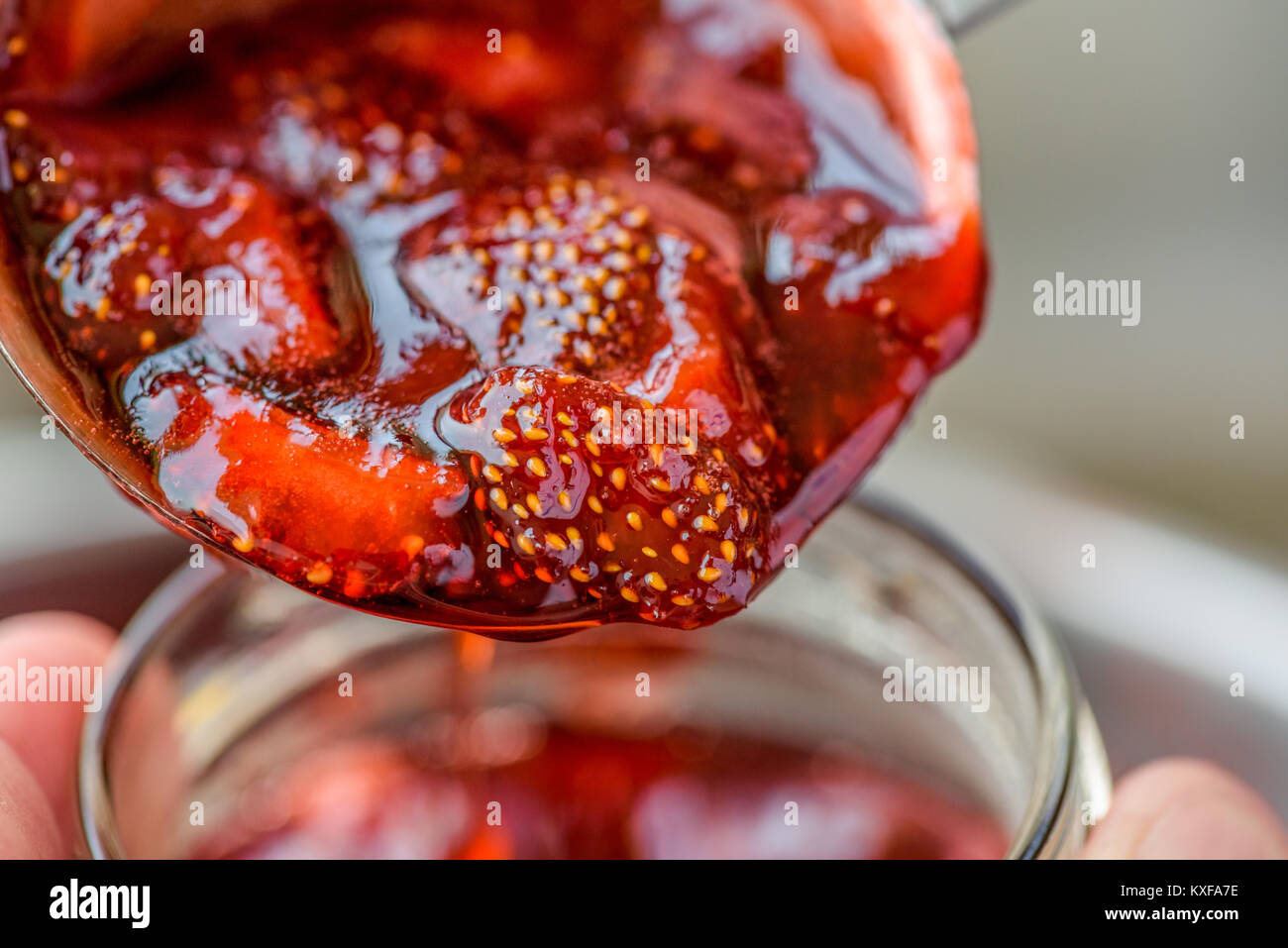 Close up di un cucchiaio colmo di fresco cotto home salsa di fragole durante il riempimento di un vasetto di vetro. Foto Stock
