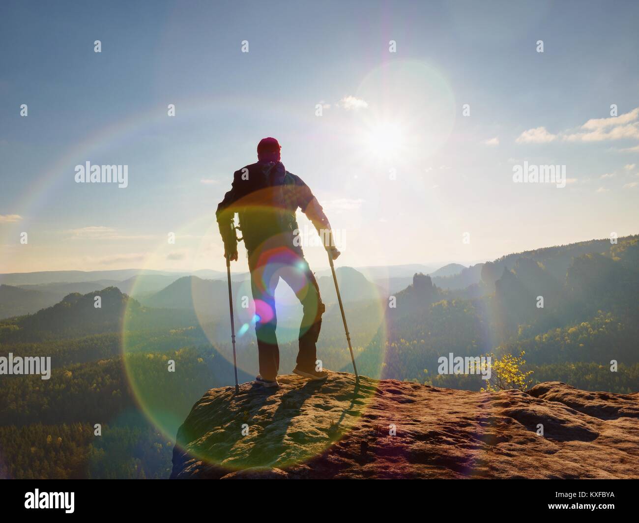 Turistico con avambraccio stampella sopra la testa sul sentiero. Hurt escursionista raggiunto il picco di montagna con ginocchio rotti in immobilizzatore. Profonda valle bellow silhouette o Foto Stock