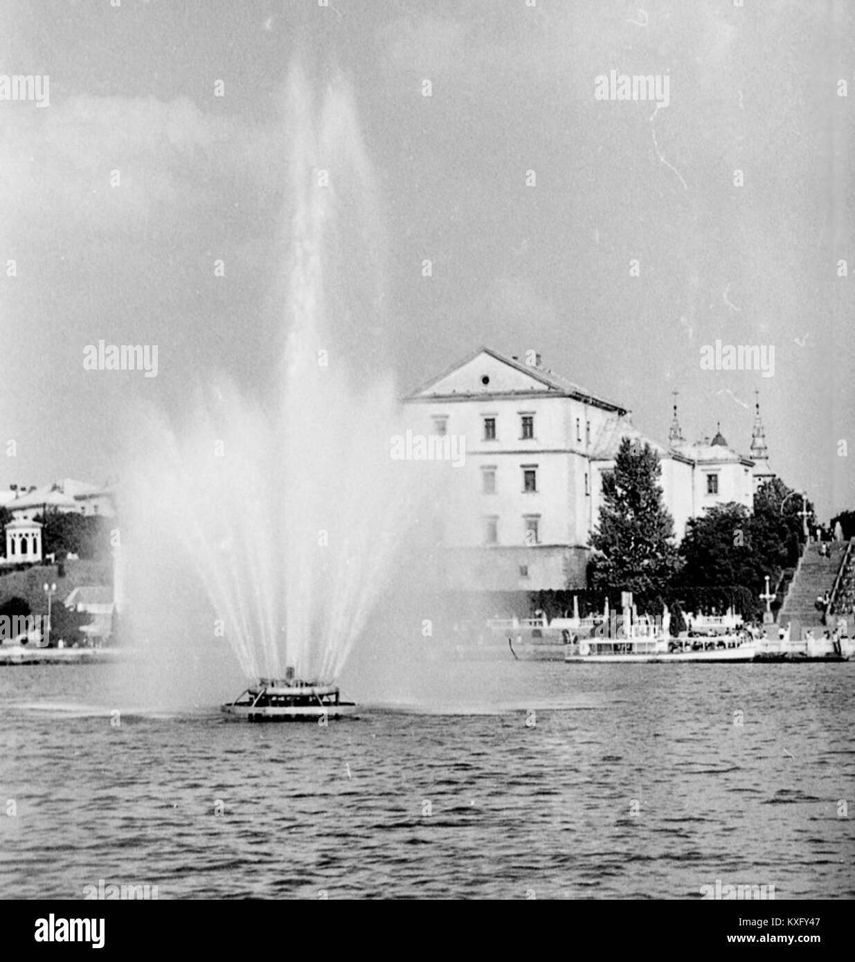 Un'immagine che mostra una vecchia fontana e il battello fluviale PT-50, probabilmente catturato in un ambiente fluviale ucraino o russo, che illustra i trasporti locali e il paesaggio urbano. Foto Stock