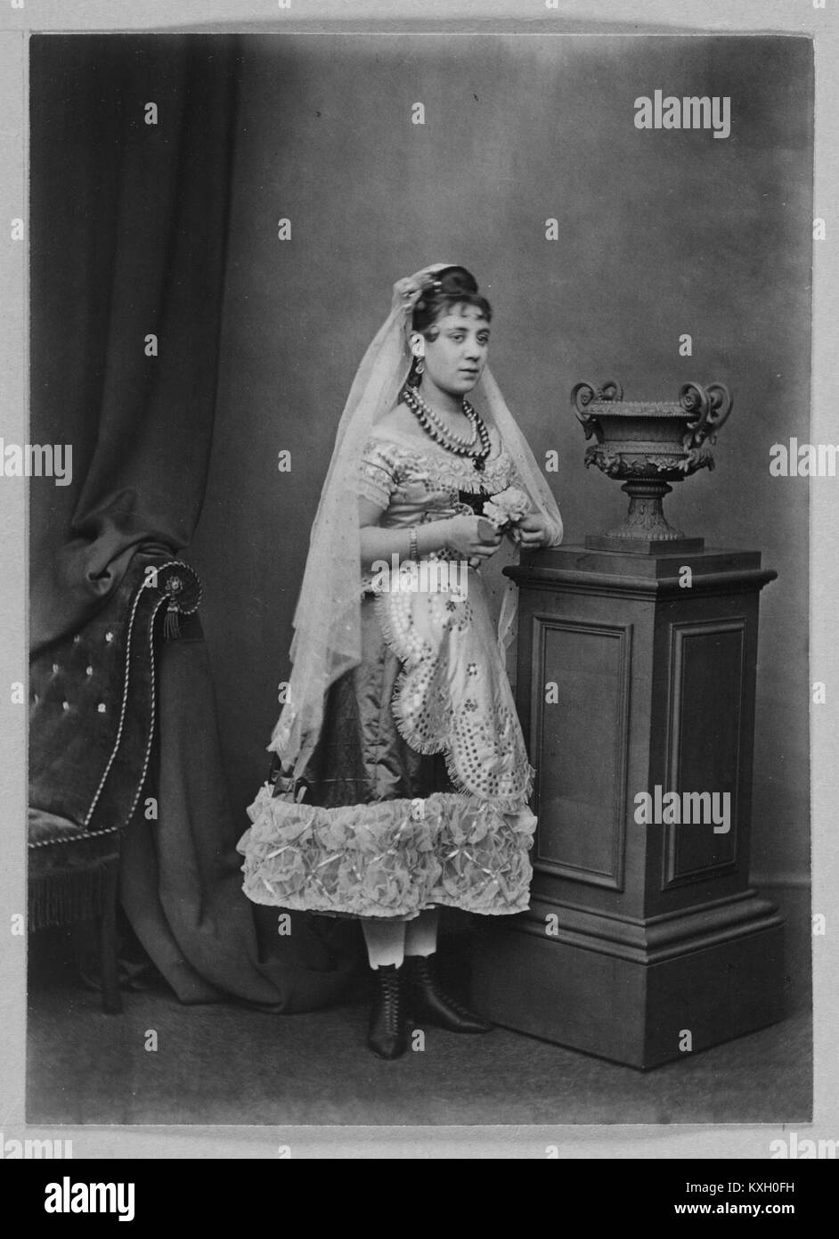 Una fotografia di un'attrice in costume posta vicino a un'urna, che mette in evidenza abiti teatrali e oggetti di scena della Weir Collection. Foto Stock