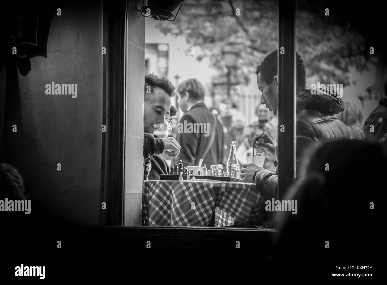 Fotografia di strada in bianco e nero scattata attraverso una finestra di vetro che cattura due uomini profondamente concentrati mentre giocano a scacchi su un panno a quadri Foto Stock