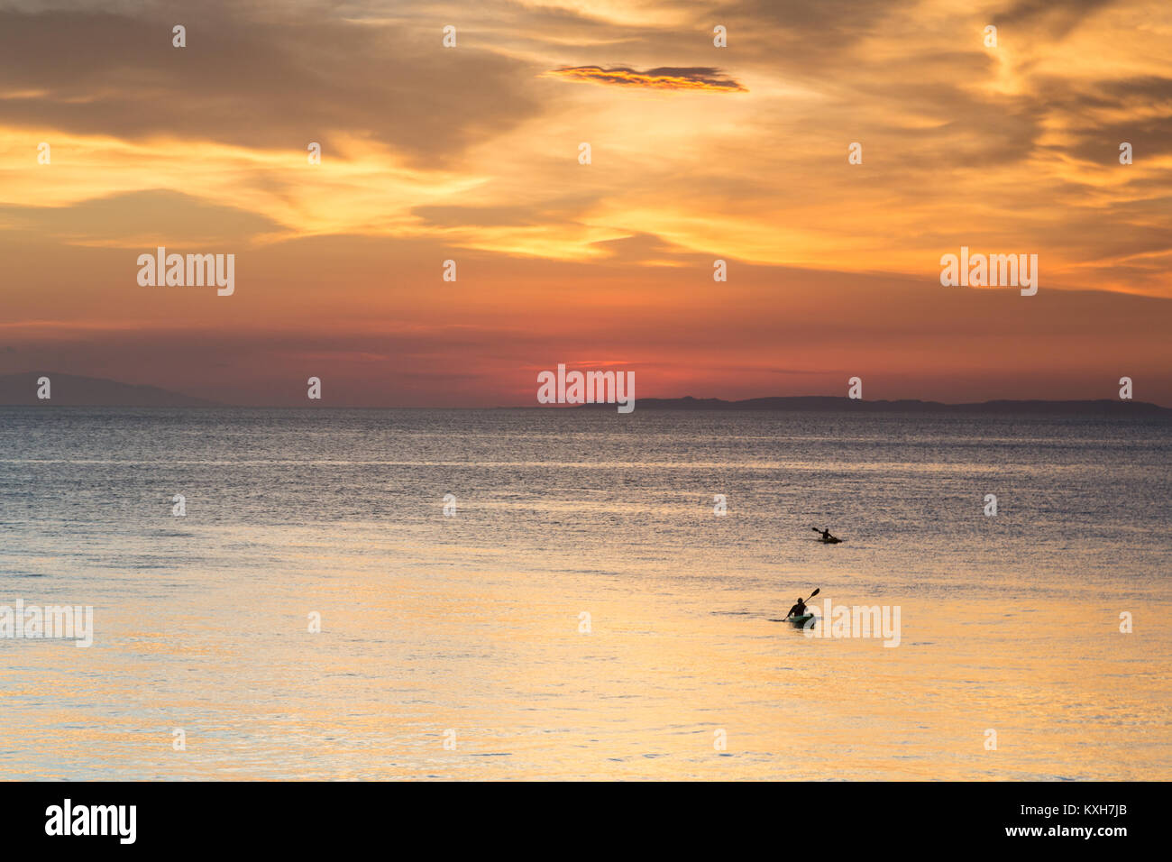Kayakers paddle attraverso il mare calmo sotto una soluzione satura di Cielo di tramonto in Anilao, Filippine. Foto Stock