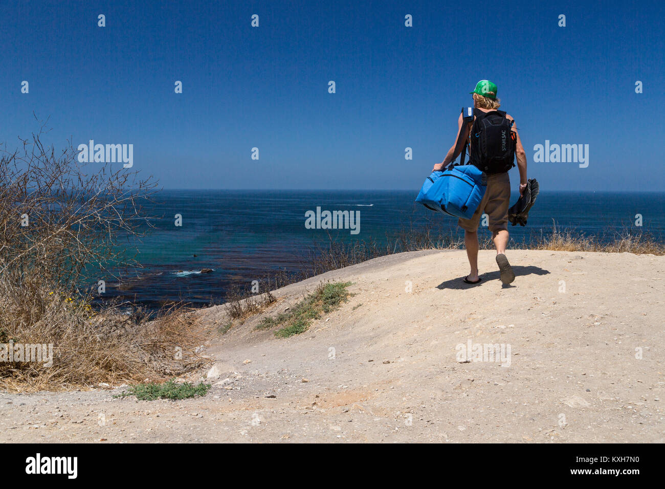 Un subacqueo porta marcia giù per un sentiero sterrato all'oceano nella California Meridionale. Foto Stock