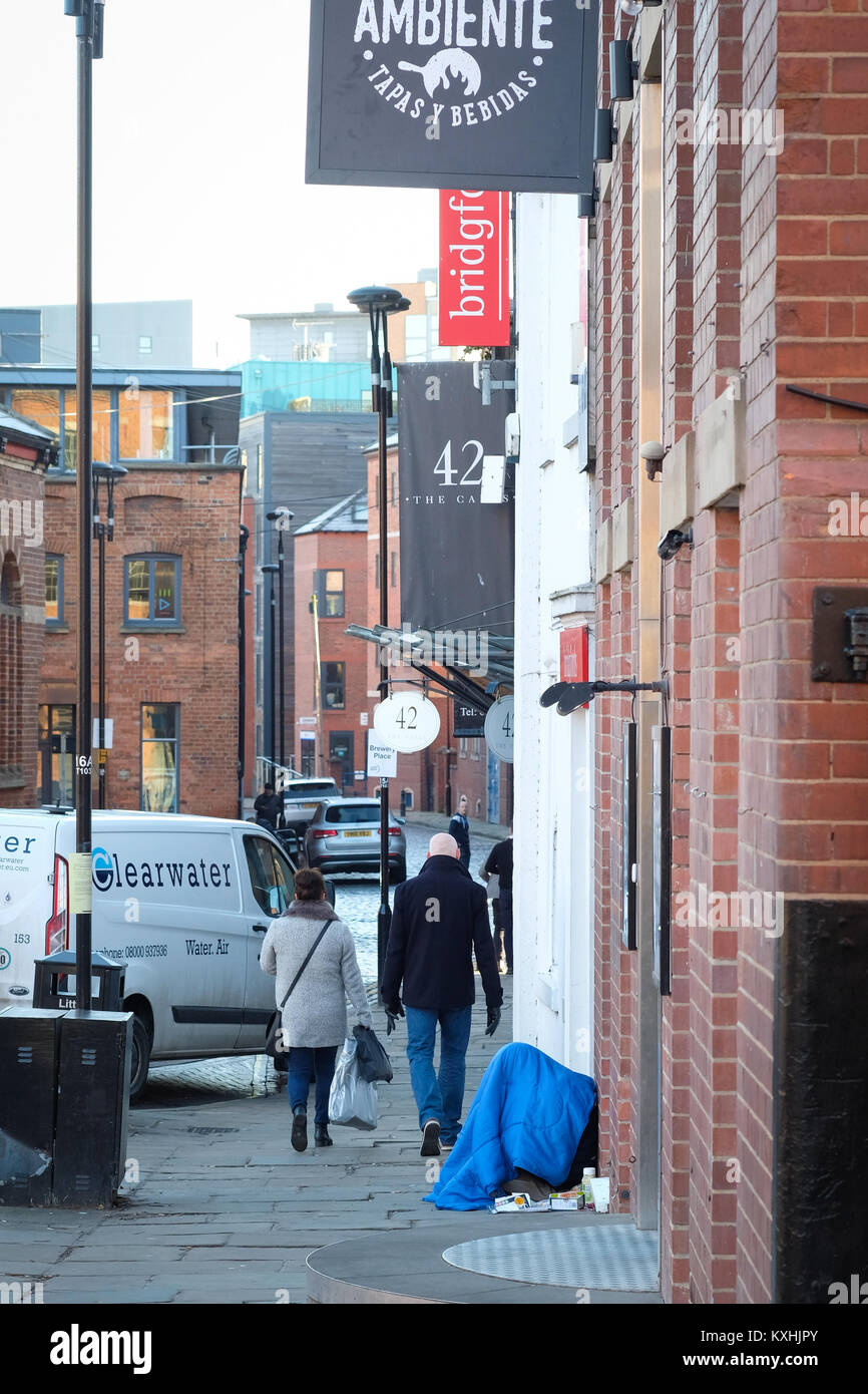 Un senzatetto mendica sul ponte centenario, Leeds, Regno Unito in inverno, come pendolari di passaggio. Regno Unito crisi di alloggiamento 2018. Il divario sociale. Foto Stock