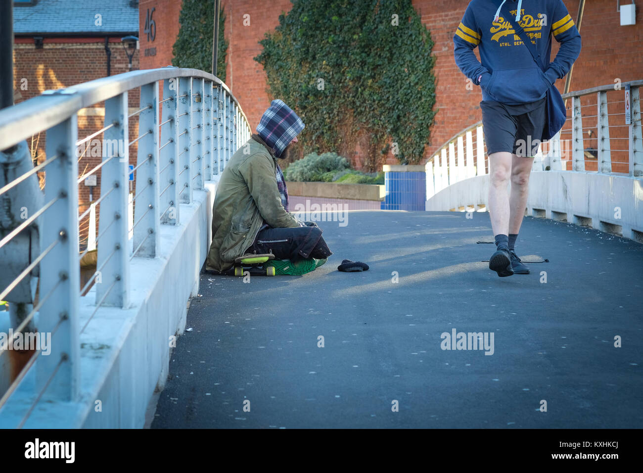 Un senzatetto mendica sul ponte centenario, Leeds, Regno Unito in inverno, come pendolari di passaggio. Regno Unito crisi di alloggiamento 2018. Il divario sociale. Foto Stock