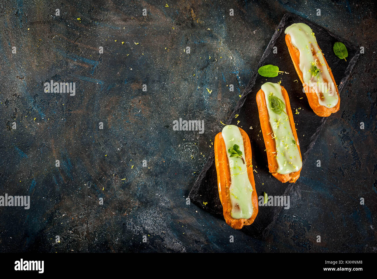 Tradizionale Francese dessert. Il Mojito Eclairs con la scorza del lime e foglie di menta, su sfondo blu scuro, spazio copia vista superiore Foto Stock