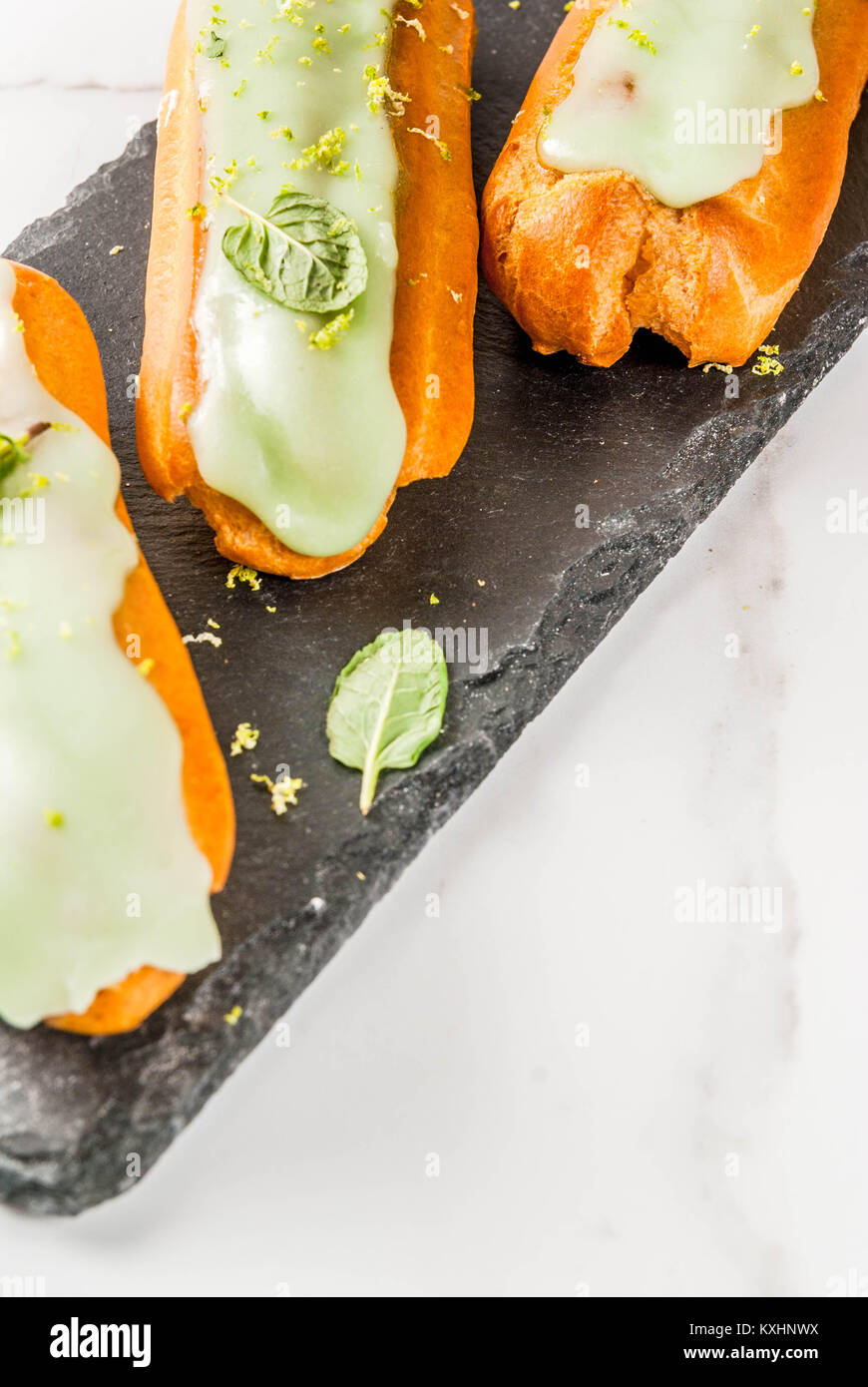 Tradizionale Francese dessert. Il Mojito Eclairs con la scorza del lime e foglie di menta, su sfondo blu scuro, spazio copia vista superiore Foto Stock