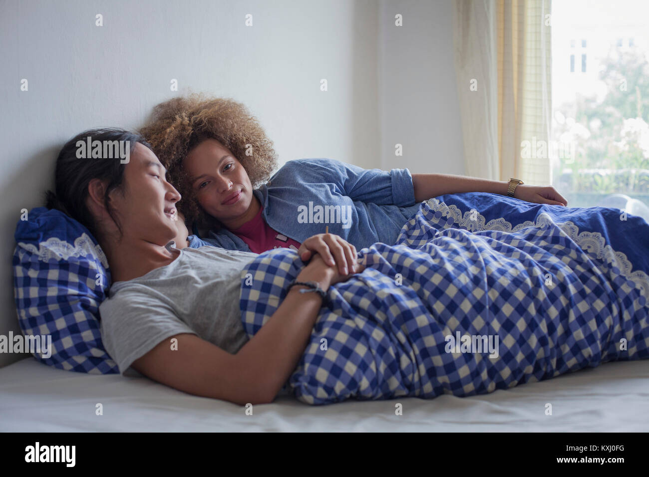 Giovane coppia sdraiata sul letto contro la parete bianca dalla finestra a casa Foto Stock